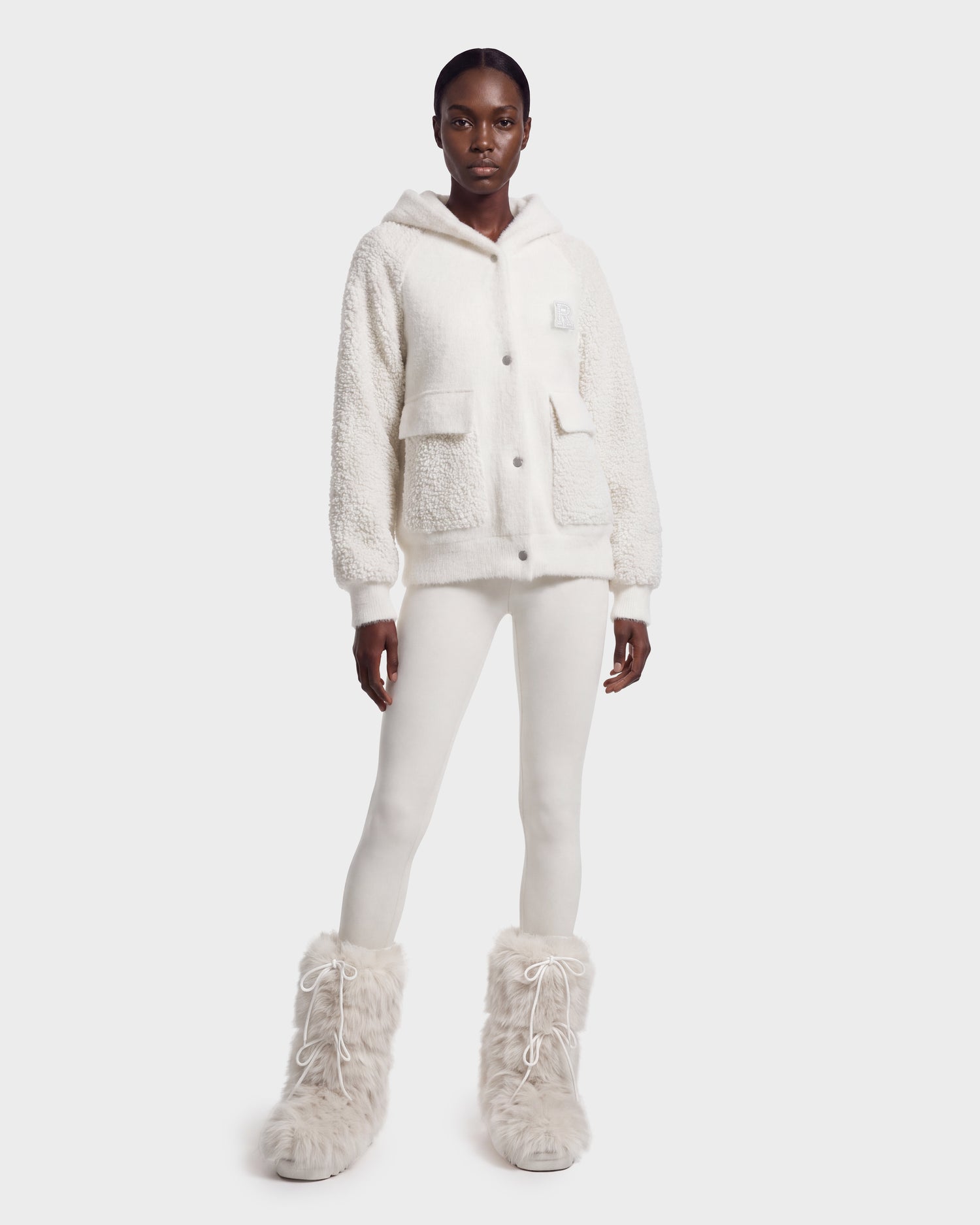 A person stands against a plain light background wearing the Rudsak DAKOTA - 8526515 Iceland cozy white sherpa hoodie, paired with white leggings and fluffy white boots.