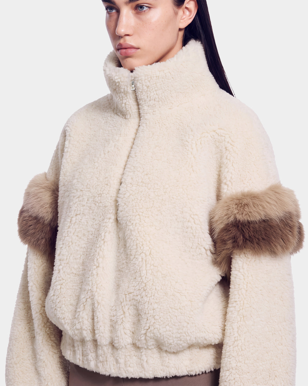 A woman wearing the Rudsak ALEIA - 8526693 Vanilla cream-colored fleece jacket with a high collar and brown faux fur accents around the upper arms, standing against a plain white background.