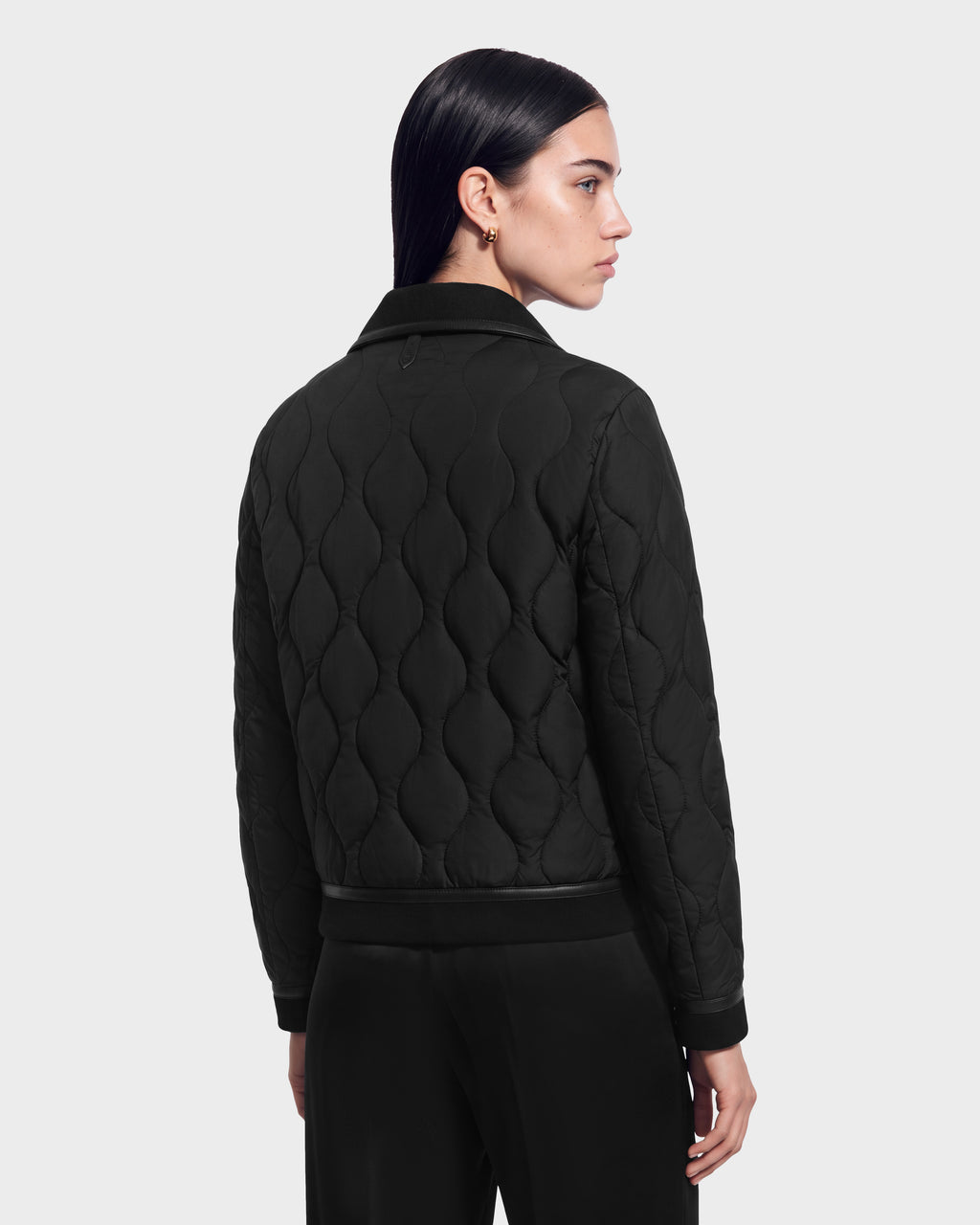 A woman viewed from the back wears a black JOLIE - 8125036 Rudsak quilted down jacket featuring a collar and ribbed trim.
