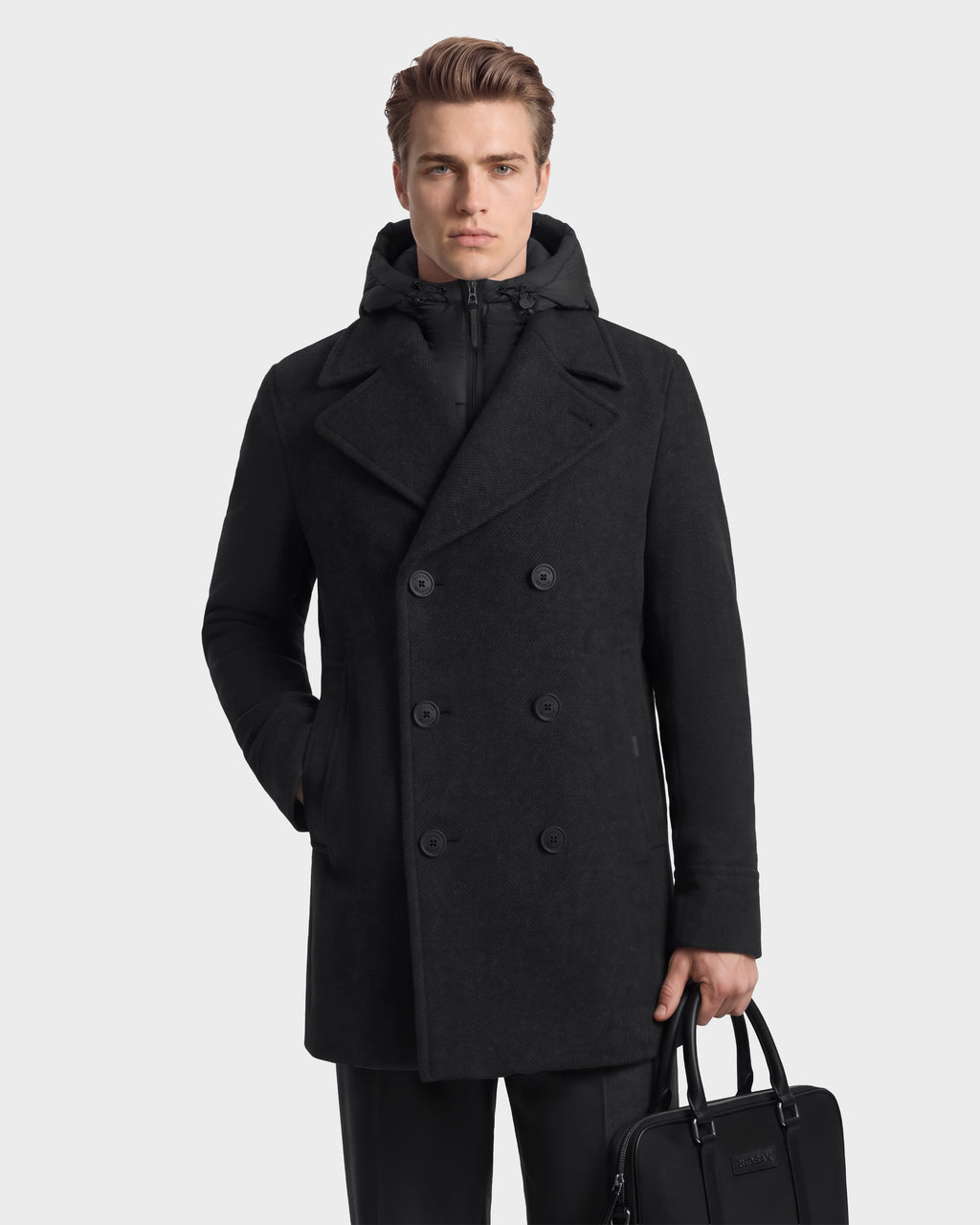 A man wearing a charcoal LUCIEN - 6126508 charcoal wool-blend pea coat with an integrated hooded vest for cold-weather performance, carrying a black briefcase.