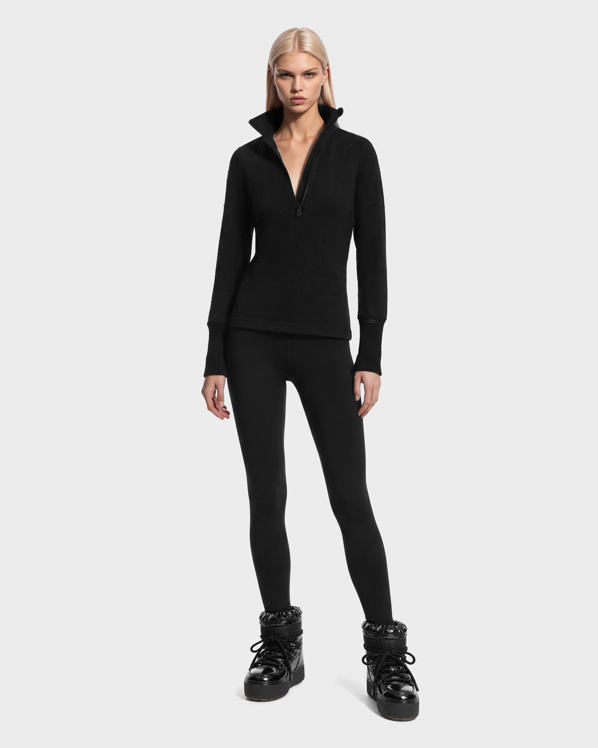 A person wearing a black quarter-zip long-sleeved top, black leggings, and NEVA - 8526524 Black high-top snow boots.