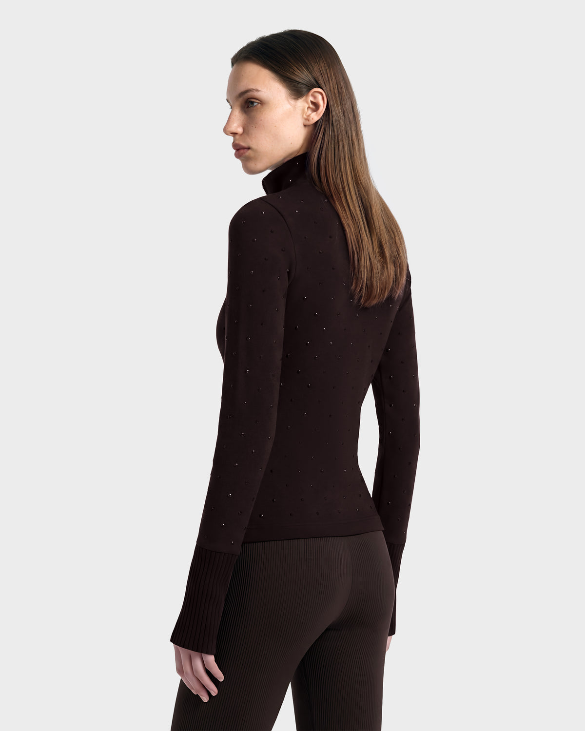 A person viewed from the back wearing the NEVA - 8526524 Espresso, a dark brown, long-sleeved après-ski turtleneck top detailed with small studs.