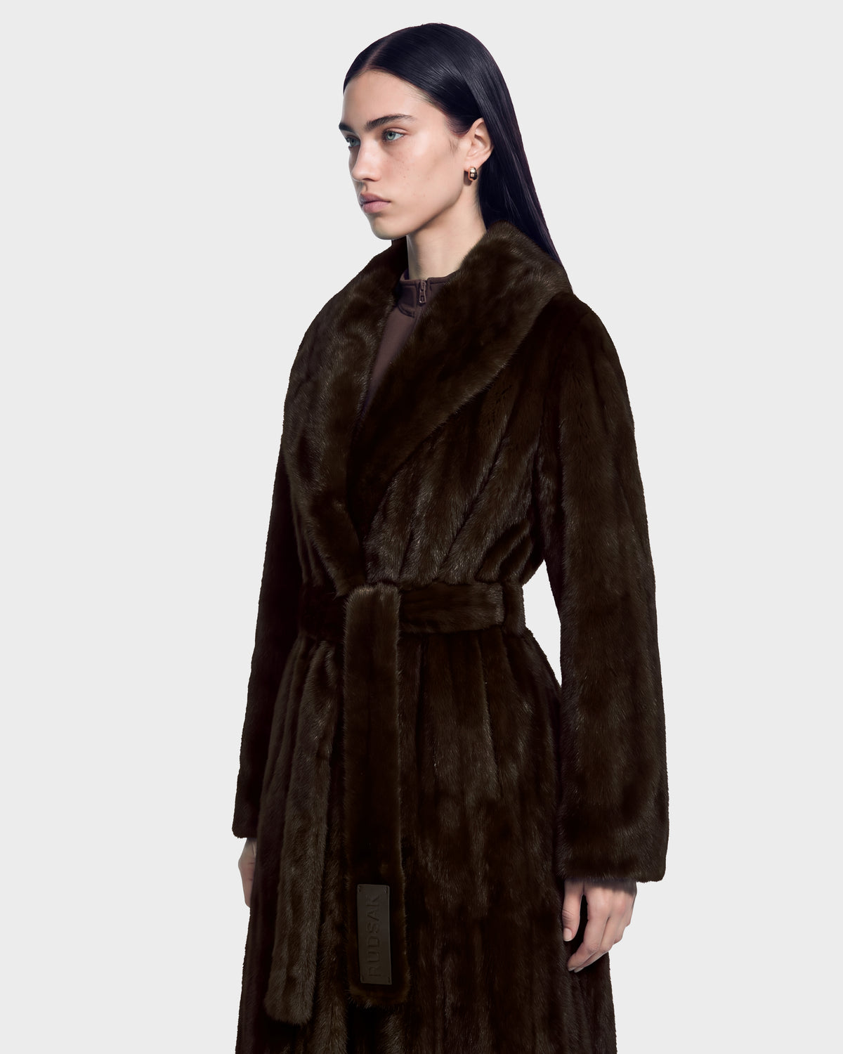 The Rudsak VIVIENNE - 8126528 Espresso is a long, dark brown faux fur coat for winter city dressing, featuring a shawl collar and a waist tie.