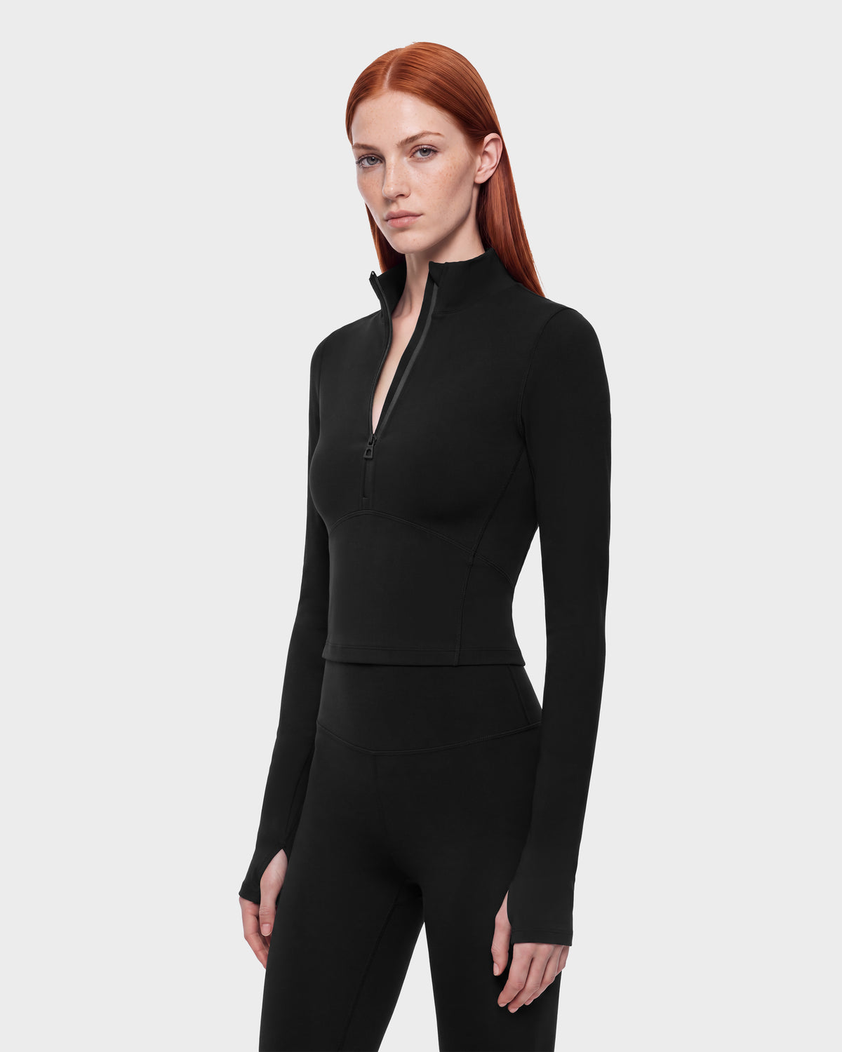 A woman wears the ANITA - 8526579 Black, a performance-inspired athletic long-sleeve top in black with a cropped silhouette, a quarter-zip mock neck, and thumb holes in the cuffs.