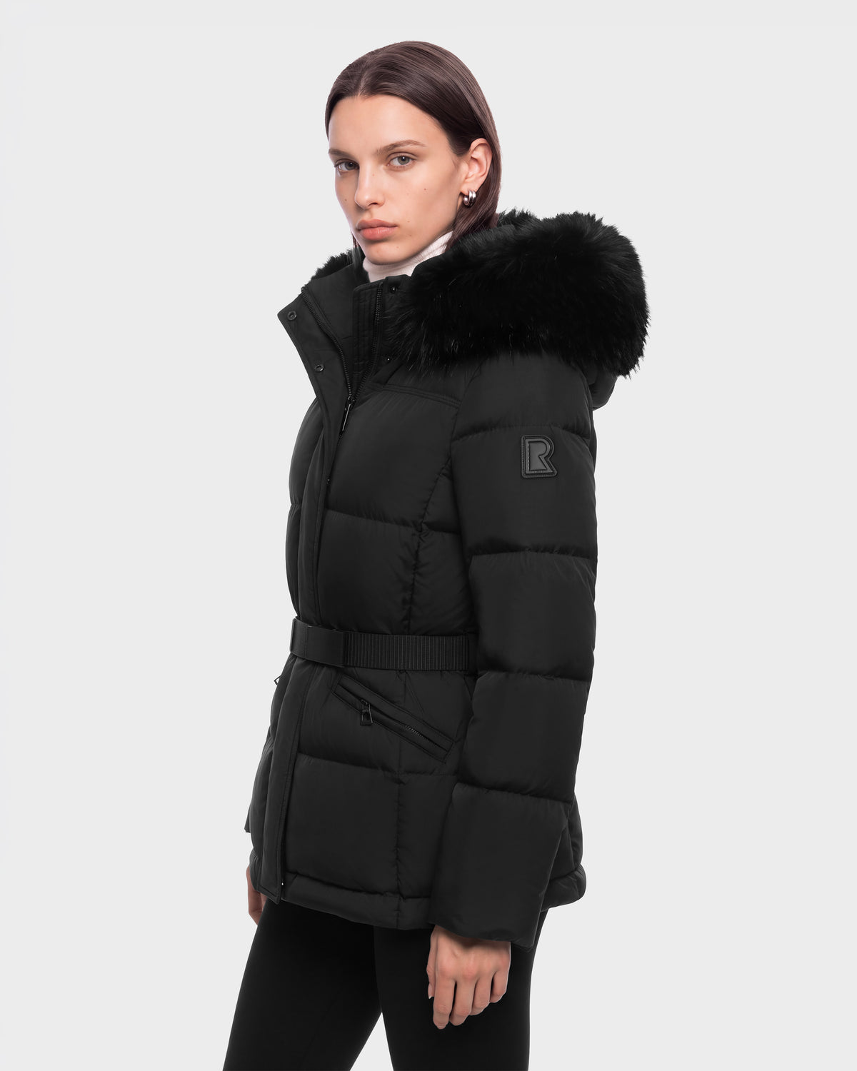 A person wears a black Rudsak GRACE FF - 8126535 puffer jacket with a belted waist and a faux-fur trimmed hood.