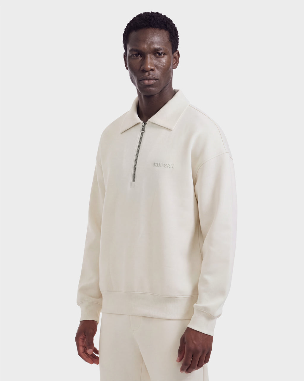 A man wearing the Rudsak IDRIS - 6526500 Vanilla quarter-zip pullover with a collar and matching pants faces forward against a plain white background.