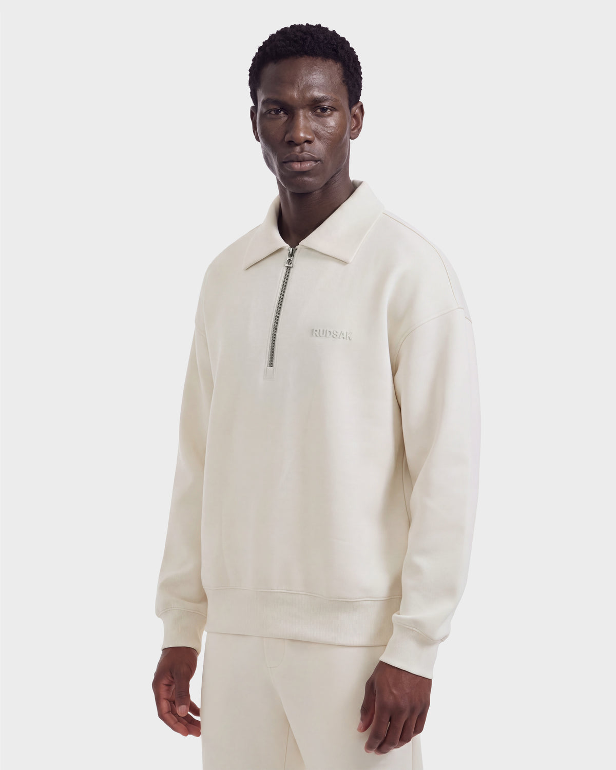 A man wearing the Rudsak IDRIS - 6526500 Vanilla quarter-zip pullover with a collar and matching pants faces forward against a plain white background.