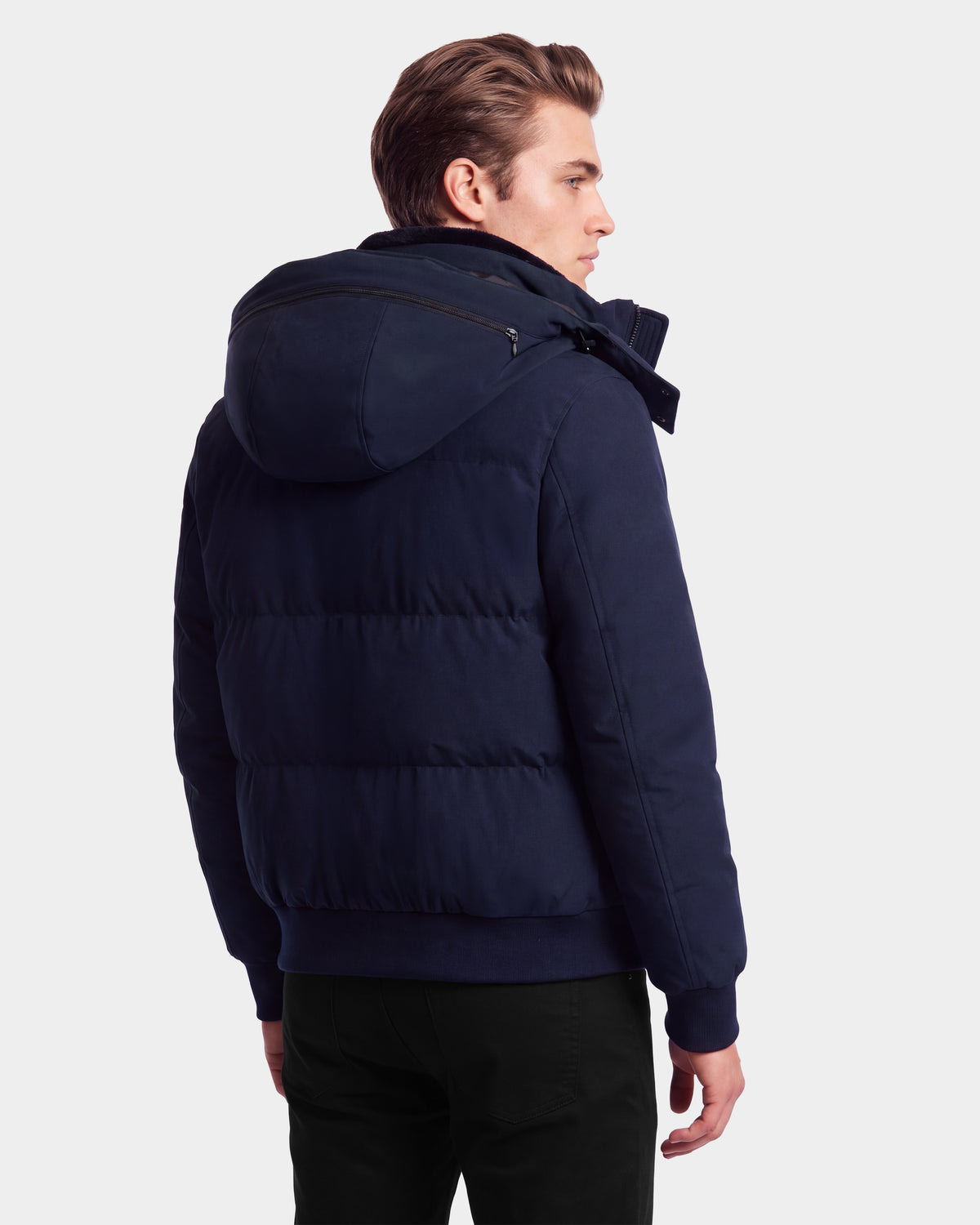 A man stands facing away, wearing the Rudsak WILL - 6126561 Navy winter coat with a hood and black pants, against a plain light background.