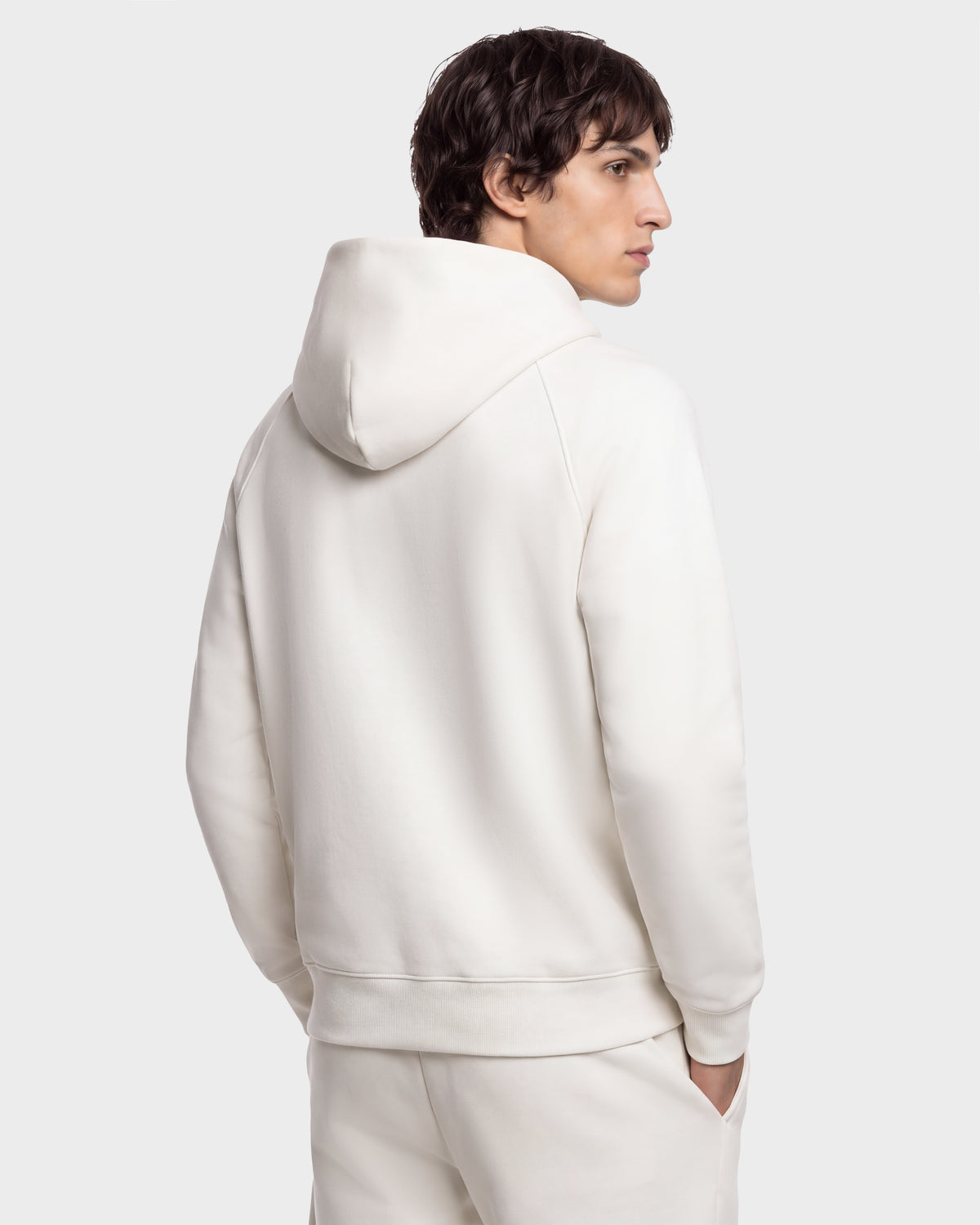 A person viewed from the back wearing a plain, cream-colored BRIAR - 9525001 Vanilla M unisex hooded sweatshirt.