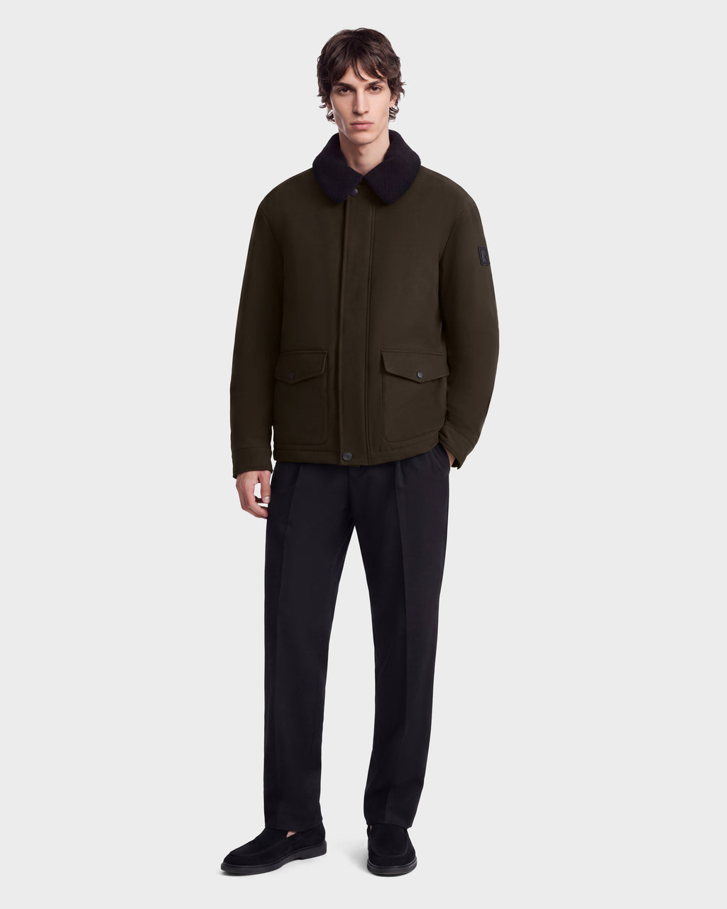 A man wearing a Rudsak ANTOINE - 6126506 Olive jacket with a dark shearling collar and black trousers.