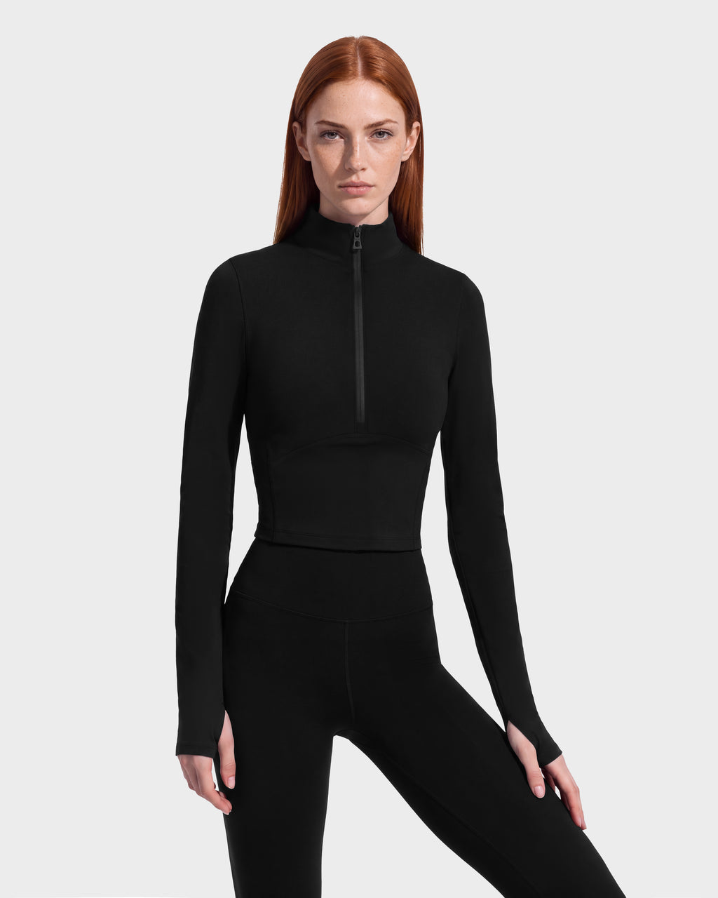 A person wears the Rudsak ANITA - 8526579 Black, a performance-inspired black long-sleeved crop top with a quarter-zip mock neck and thumbhole cuffs.