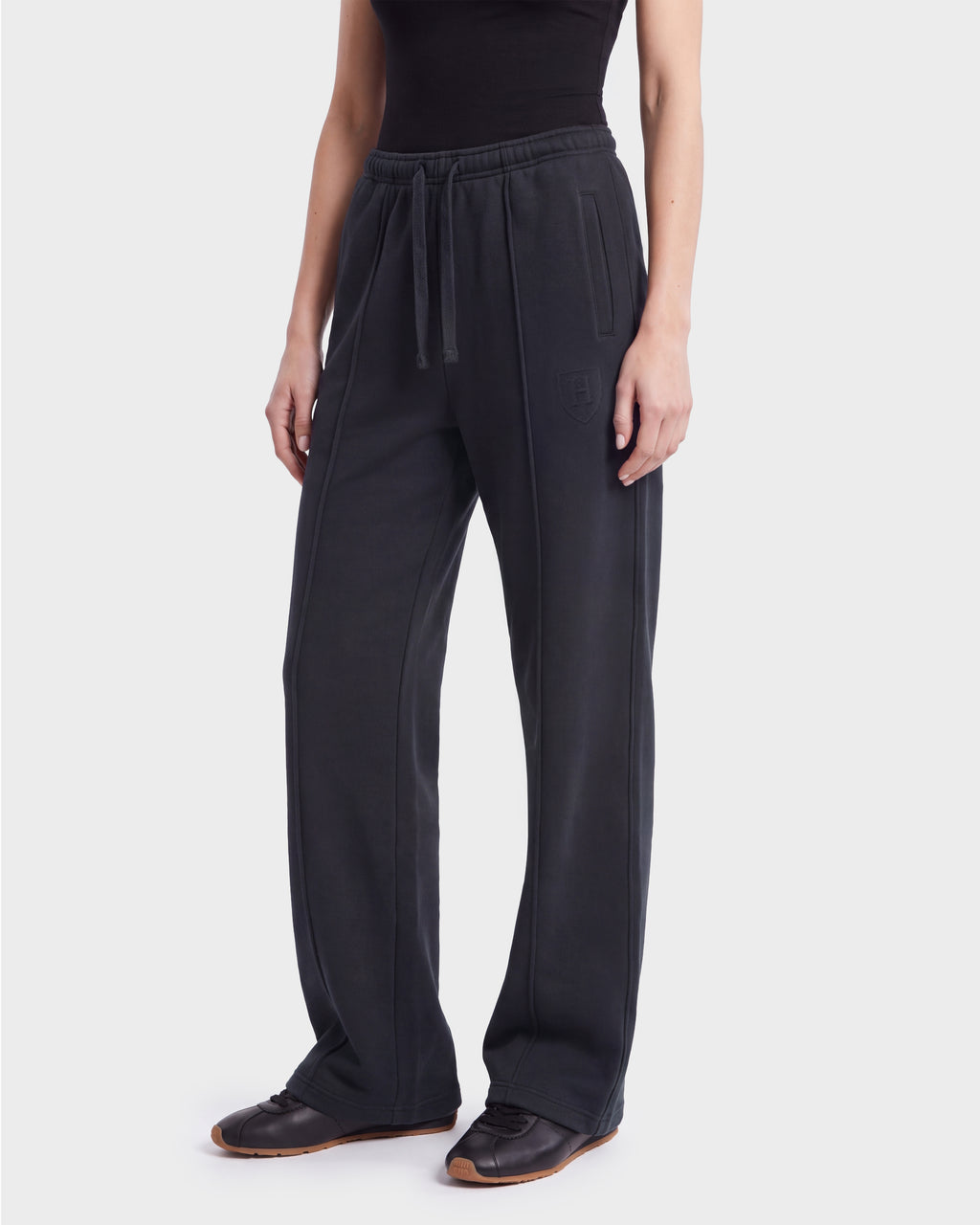 A person wearing Rudsak’s GAELLE HV - H526902 Titanium jogger sweatpants in black, featuring a heavyweight jersey fabric, elastic waistband, drawstring closure, and side pockets, is paired with a black top and black sneakers while standing against a plain white background.