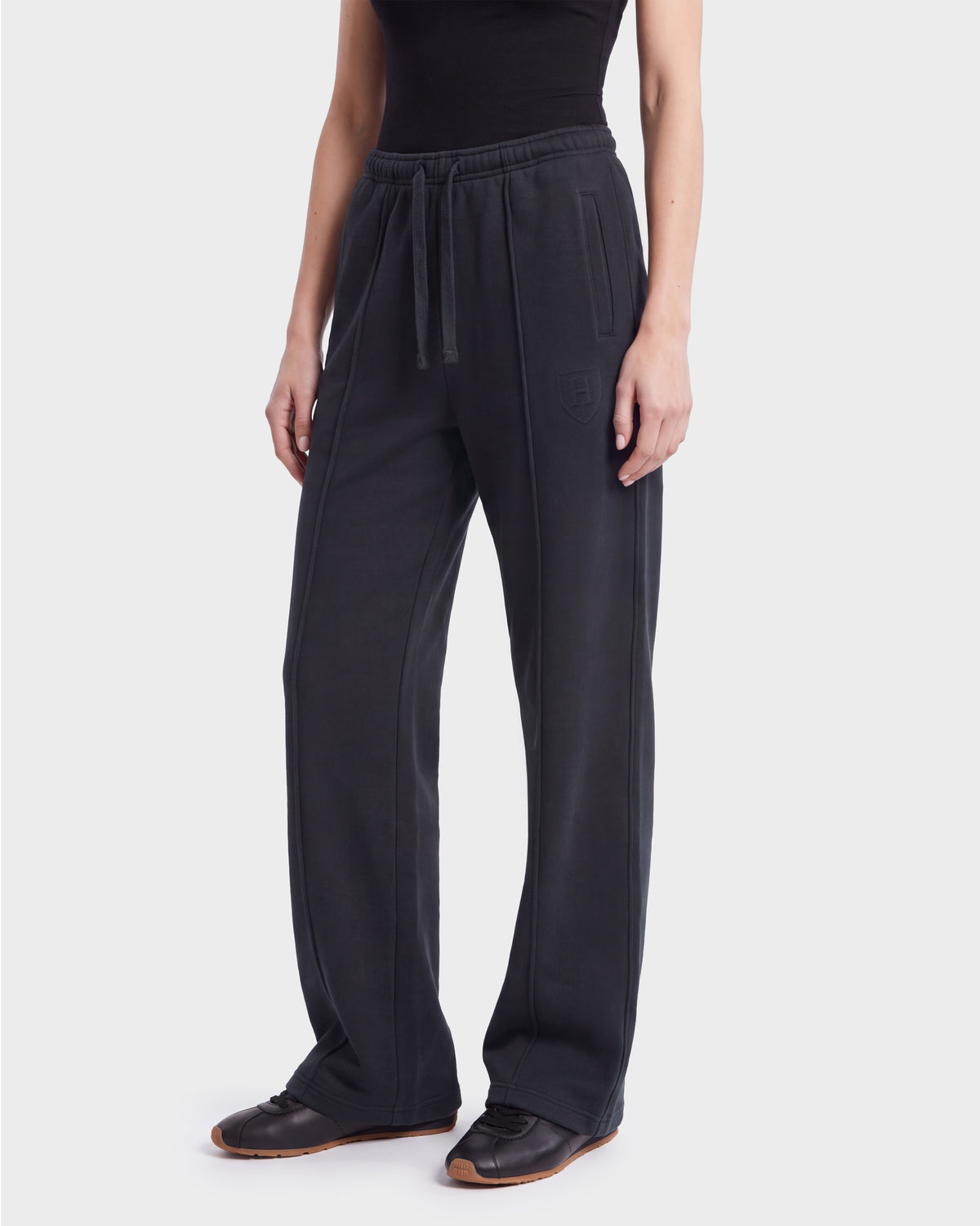 A person wearing Rudsak’s GAELLE HV - H526902 Titanium jogger sweatpants in black, featuring a heavyweight jersey fabric, elastic waistband, drawstring closure, and side pockets, is paired with a black top and black sneakers while standing against a plain white background.