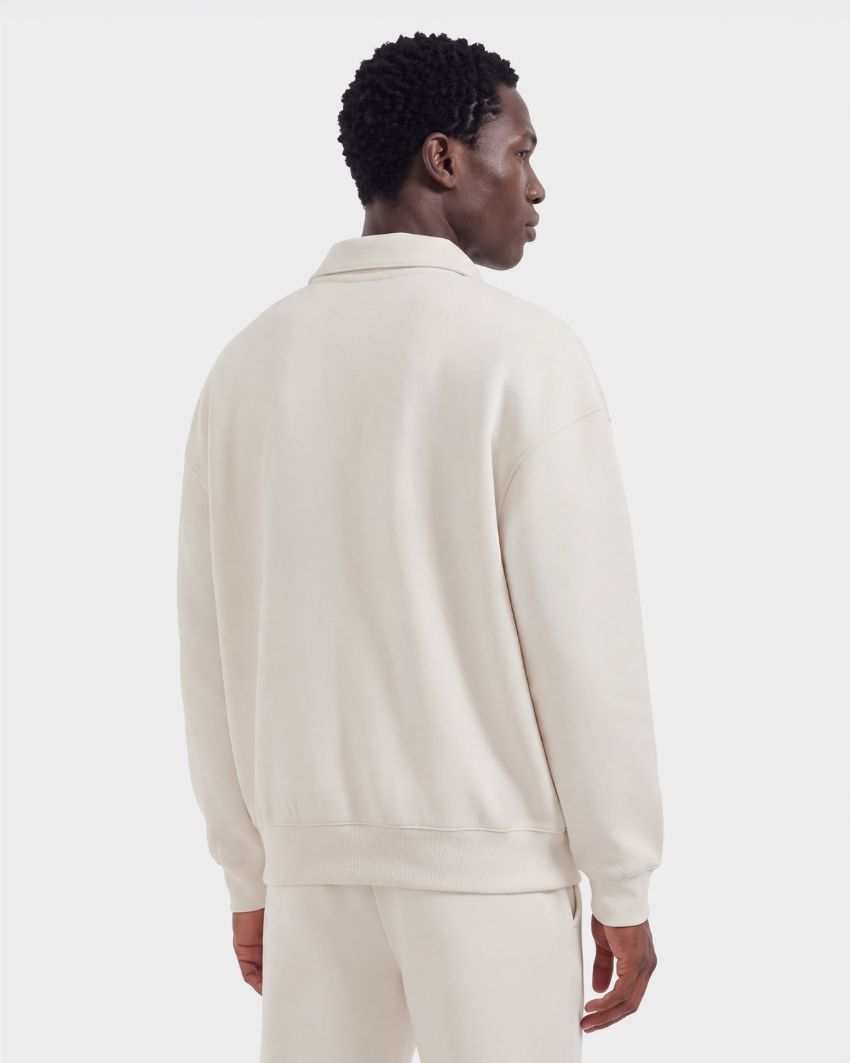 A man, seen from behind, wears the Rudsak IDRIS - 6526500 Vanilla set—an off-white, long-sleeve collared sweatshirt and matching pants—against a plain white background.