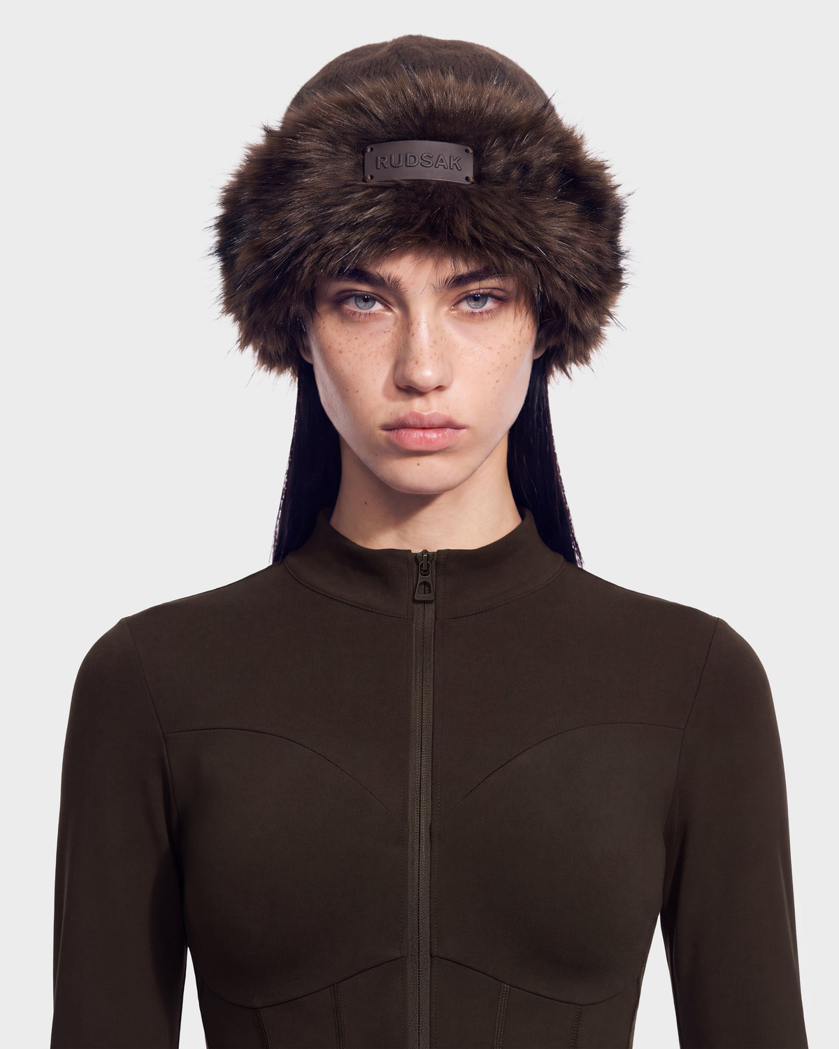 A person wearing a dark brown LORETTA W - 8426510 Espresso faux fur ushanka hat with a small logo patch on the front.