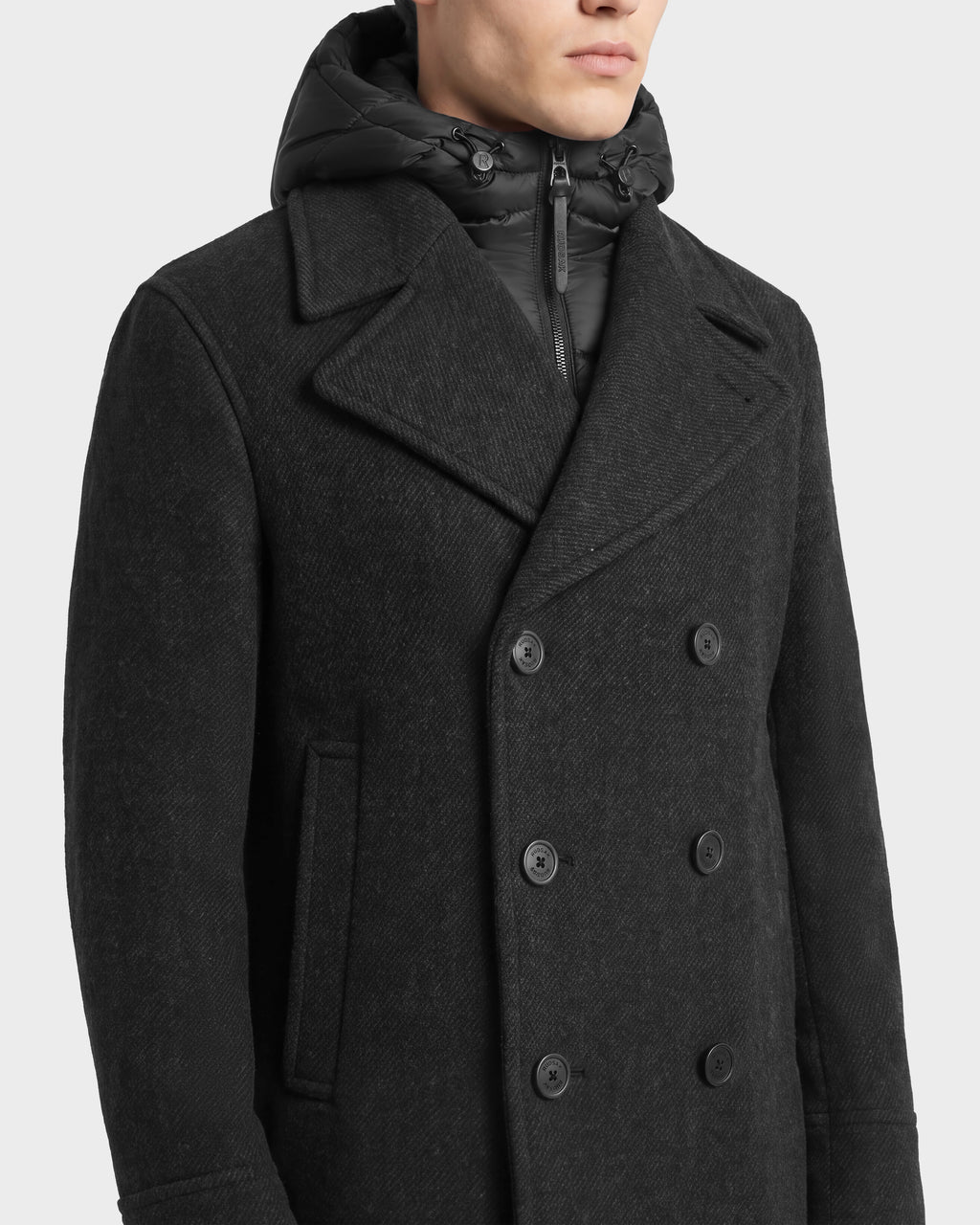 A person wearing a Rudsak LUCIEN - 6126508 Charcoal double-breasted pea coat in charcoal wool-blend with a black duck down insulated hood.