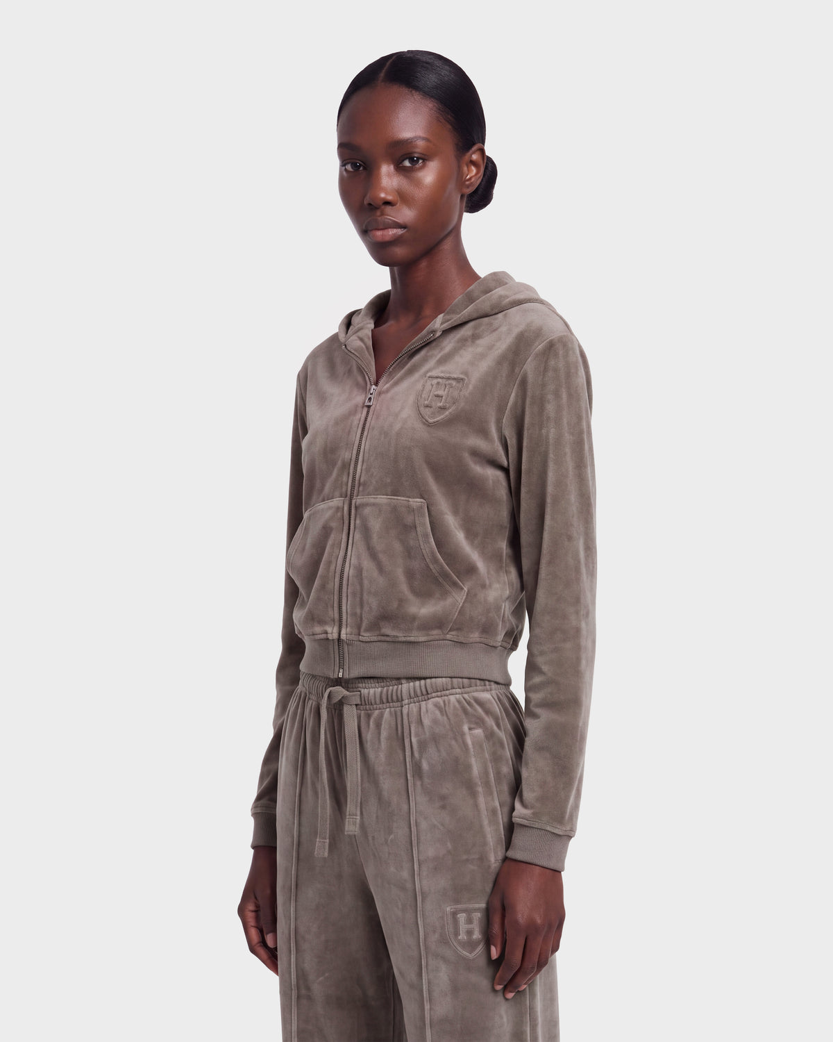 A person wearing the Rudsak TYRA HV - H526904 Taupe velour hoodie and drawstring pants stands against a plain light background, looking forward with a neutral expression.