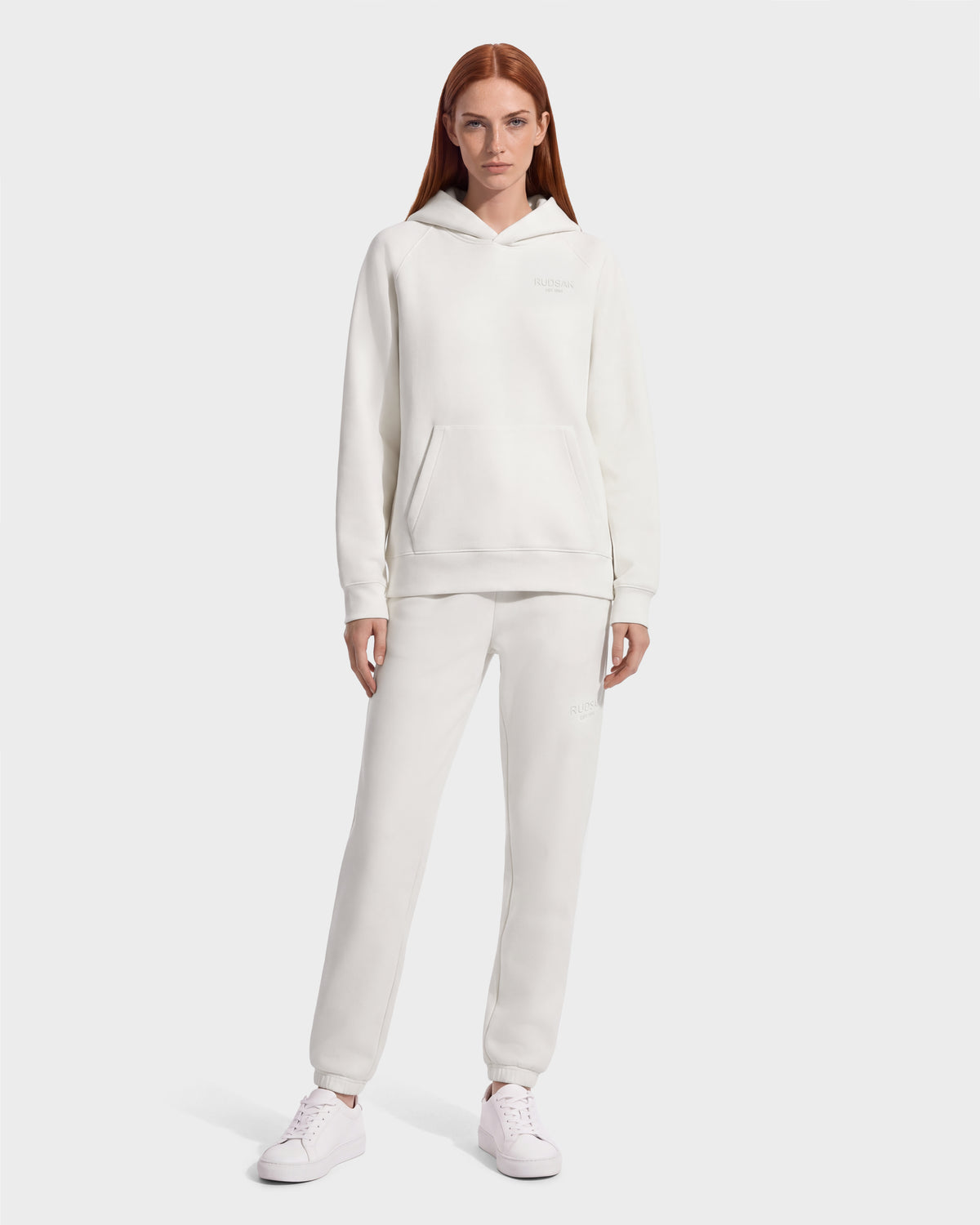 A person wearing a matching off-white BRIAR - 9525001 Vanilla W unisex hoodie and sweatpants with white sneakers for a casual look.