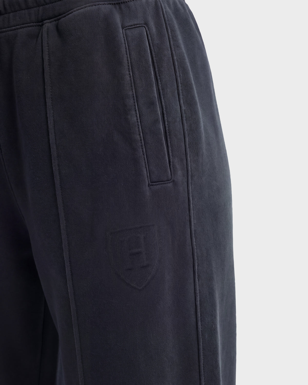 Close-up of the GAELLE HV - H526902 Titanium heavyweight jersey jogger sweatpants by Rudsak, featuring a vertical side pocket and an embossed shield emblem with the letter H on the upper thigh. The background is light gray.