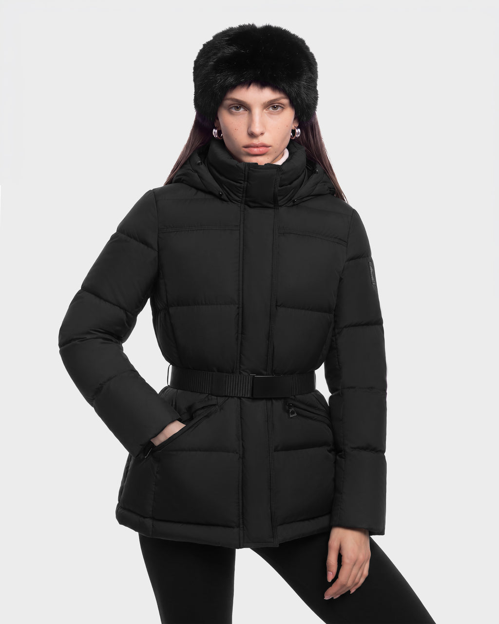 A person wearing a black Rudsak GRACE FF - 8126535 Black puffer jacket with a belted waist and a black faux-fur hat.
