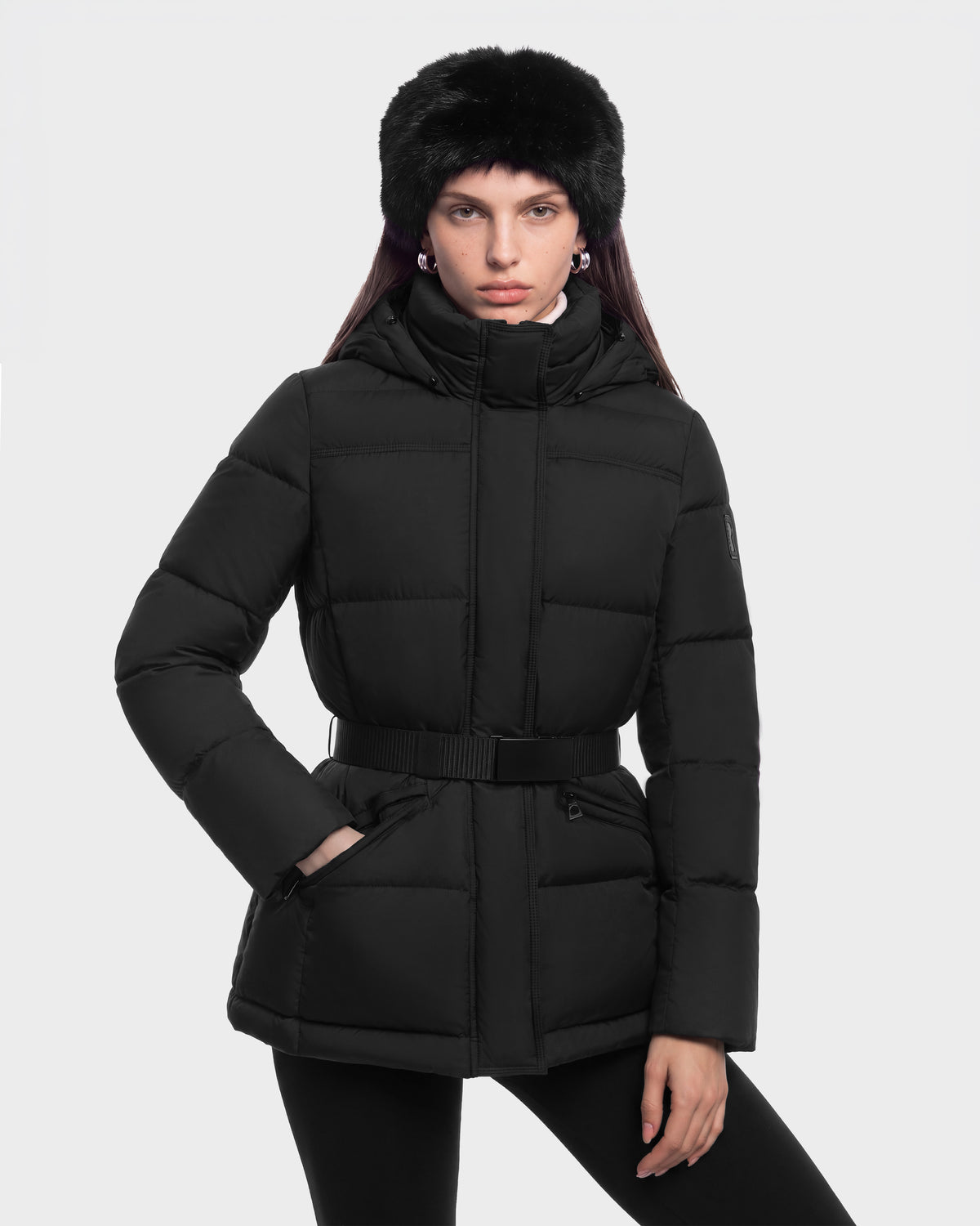 A person wearing a black Rudsak GRACE FF - 8126535 Black puffer jacket with a belted waist and a black faux-fur hat.
