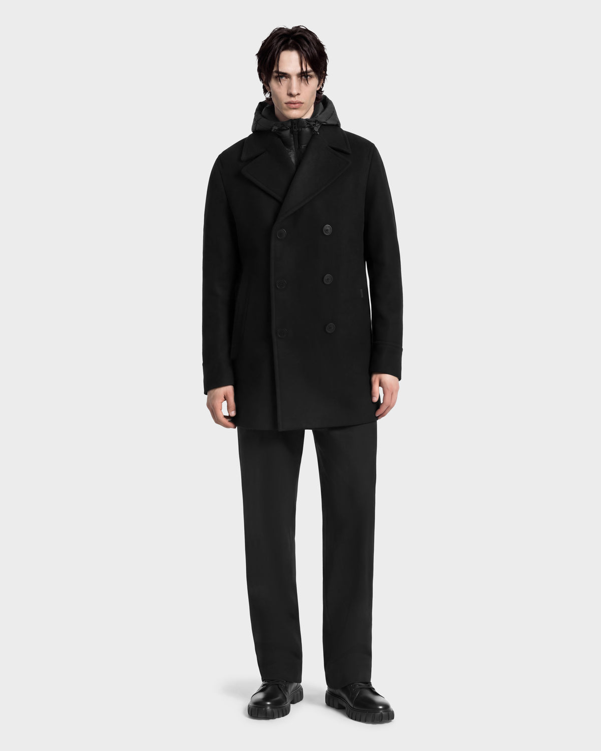A man wearing a black Rudsak LUCIEN - 6126508 Black wool-blend pea coat with a hooded inner layer, black trousers, and black leather shoes designed for cold-weather performance.