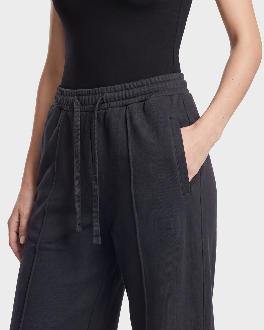 A person wearing a fitted black top and high-waisted Rudsak GAELLE HV - H526902 Titanium heavyweight jersey jogger sweatpants, with one hand in the pocket. A small shield emblem is visible on these limited-edition Rudsak sweatpants.