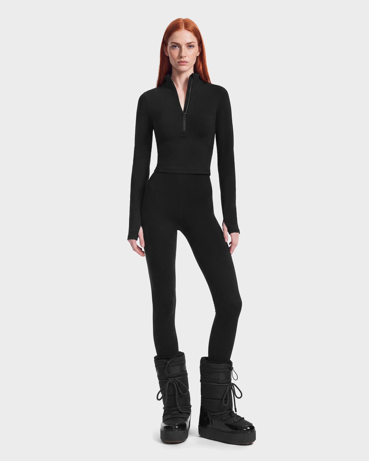 A woman wearing an ANITA - 8526579 Black athletic long-sleeve quarter-zip top, black leggings, and black winter boots.