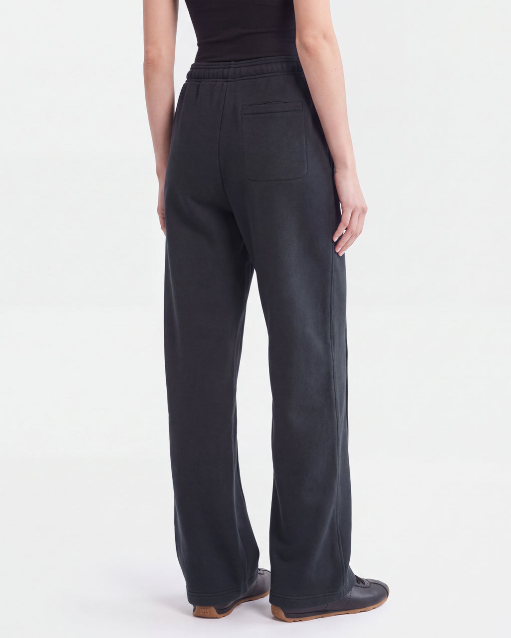 A person stands facing away against a plain white background, showcasing the back pockets of the loose-fitting, limited-edition Rudsak GAELLE HV - H526902 Titanium black pants, paired with a black sleeveless top.