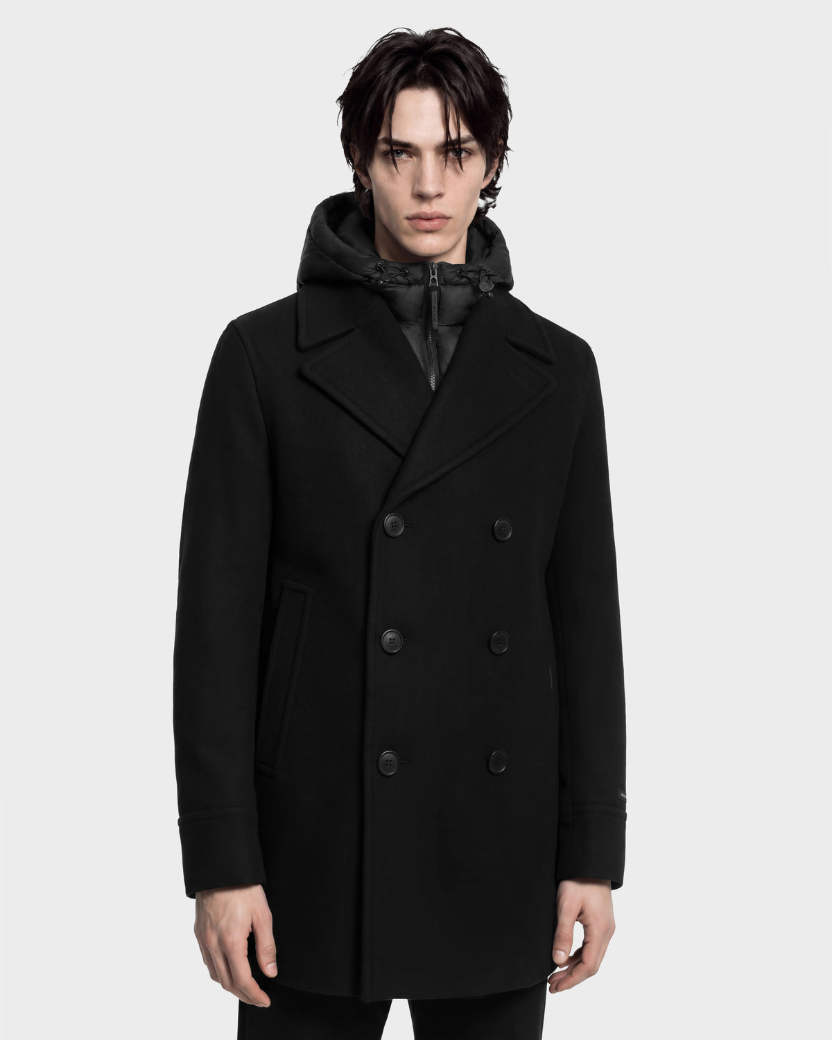 Man wearing a black LUCIEN - 6126508 Black wool-blend double-breasted pea coat with a built-in insulated hood.