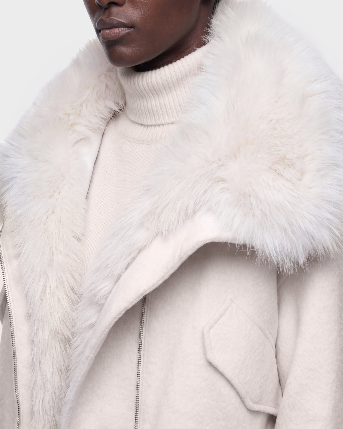 A person wearing the Rudsak ZARIA - 8126999 Vanilla cream-colored turtleneck sweater and a matching coat featuring a large, fluffy faux fur collar.