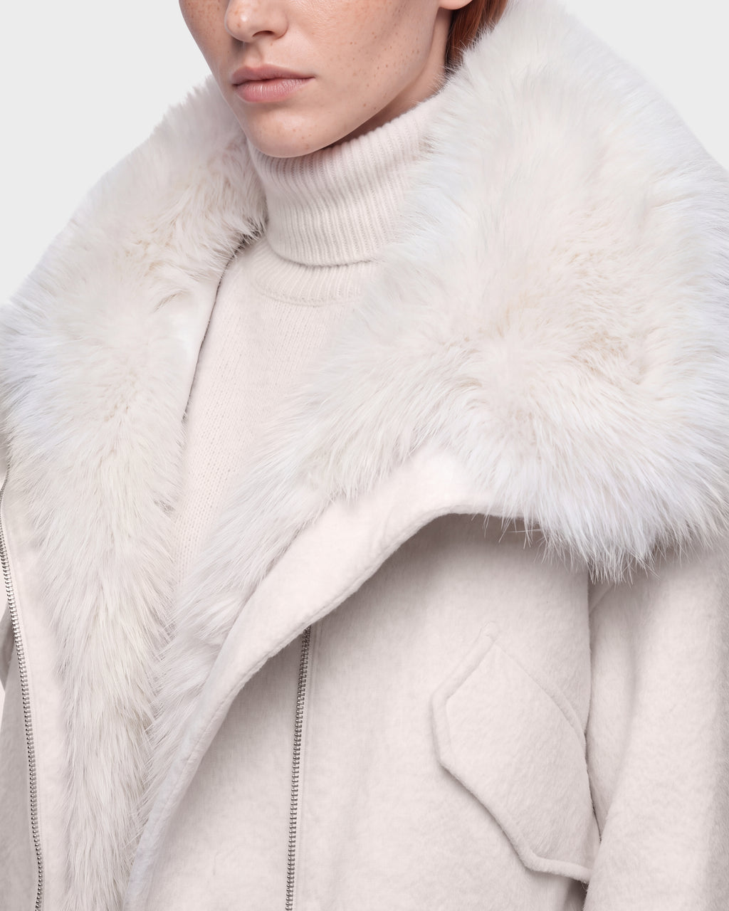 A person wearing the Rudsak ZARIA - 8126999 Vanilla cream turtleneck sweater and a light-colored winter puffer with a large, fluffy faux-fur collar. Only their lower face and upper torso are visible.