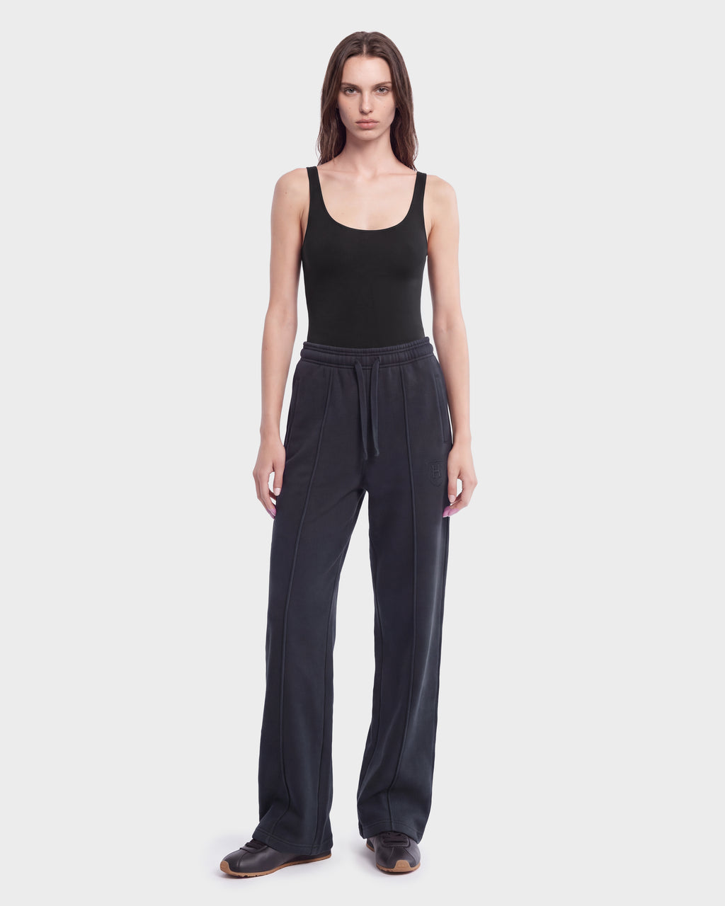 A person stands facing forward against a plain white background, wearing the Rudsak GAELLE HV - H526902 Titanium heavyweight jersey jogger pants with a drawstring, paired with a black tank top and dark shoes.