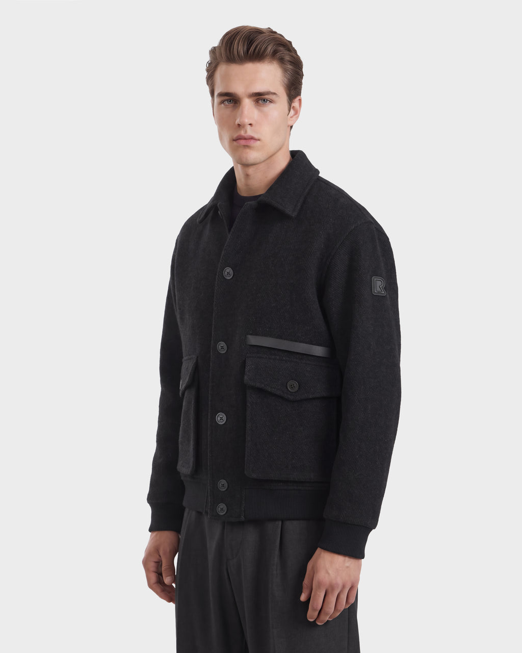 A man wears a charcoal JULIUS - 6126723 Charcoal button-up jacket with a collar, two front flap pockets, and ribbed trim at the cuffs and hem.