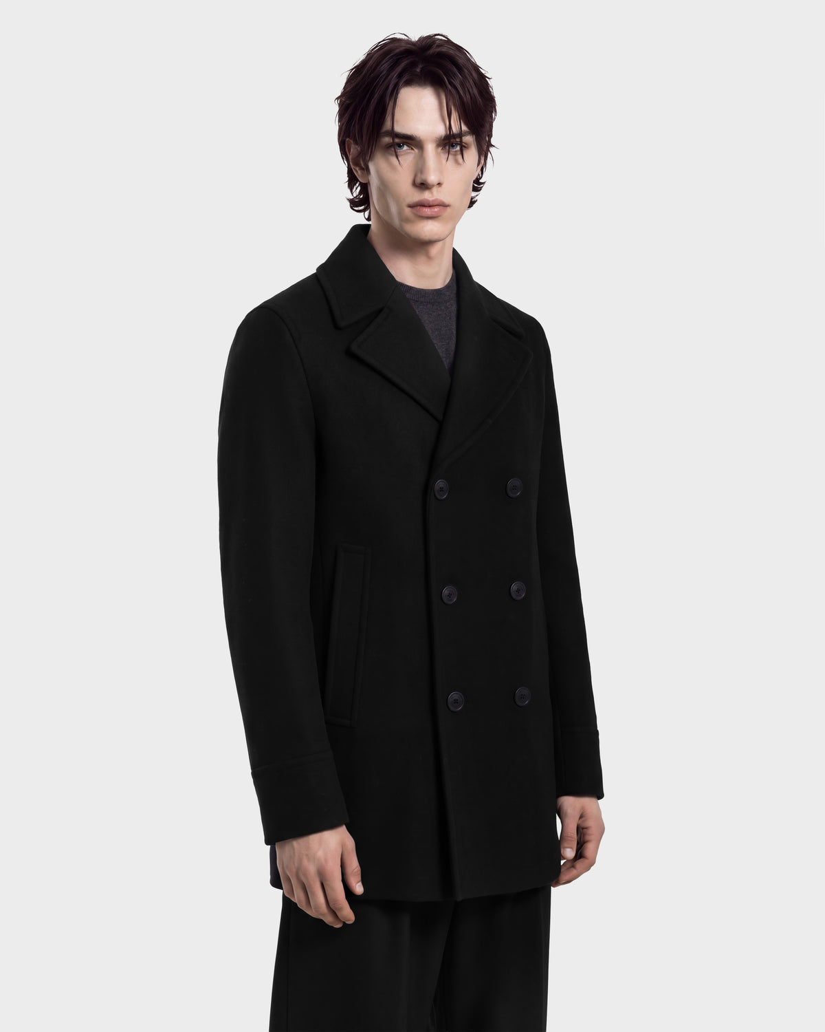 A man wears the RUDSAK LUCIEN - 6126508 Black wool-blend, double-breasted pea coat featuring wide lapels and button closures.