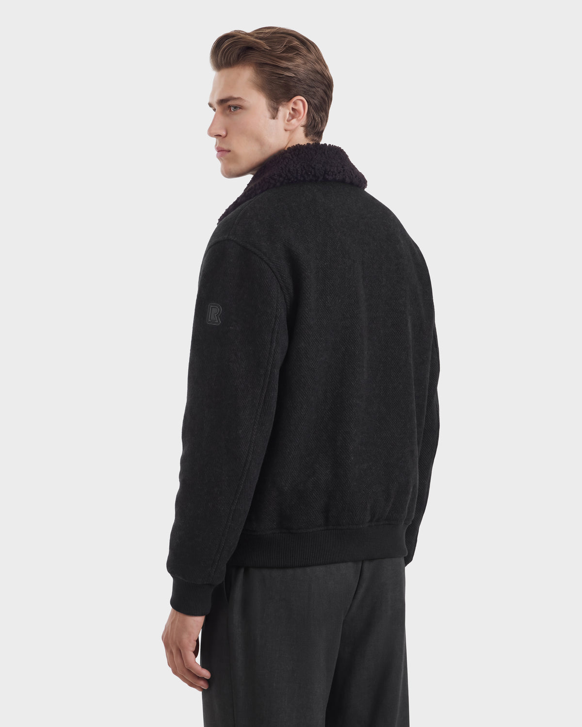 A person wearing a charcoal JULIUS - 6126723 bomber jacket with a dark faux-fur collar and ribbed cuffs.