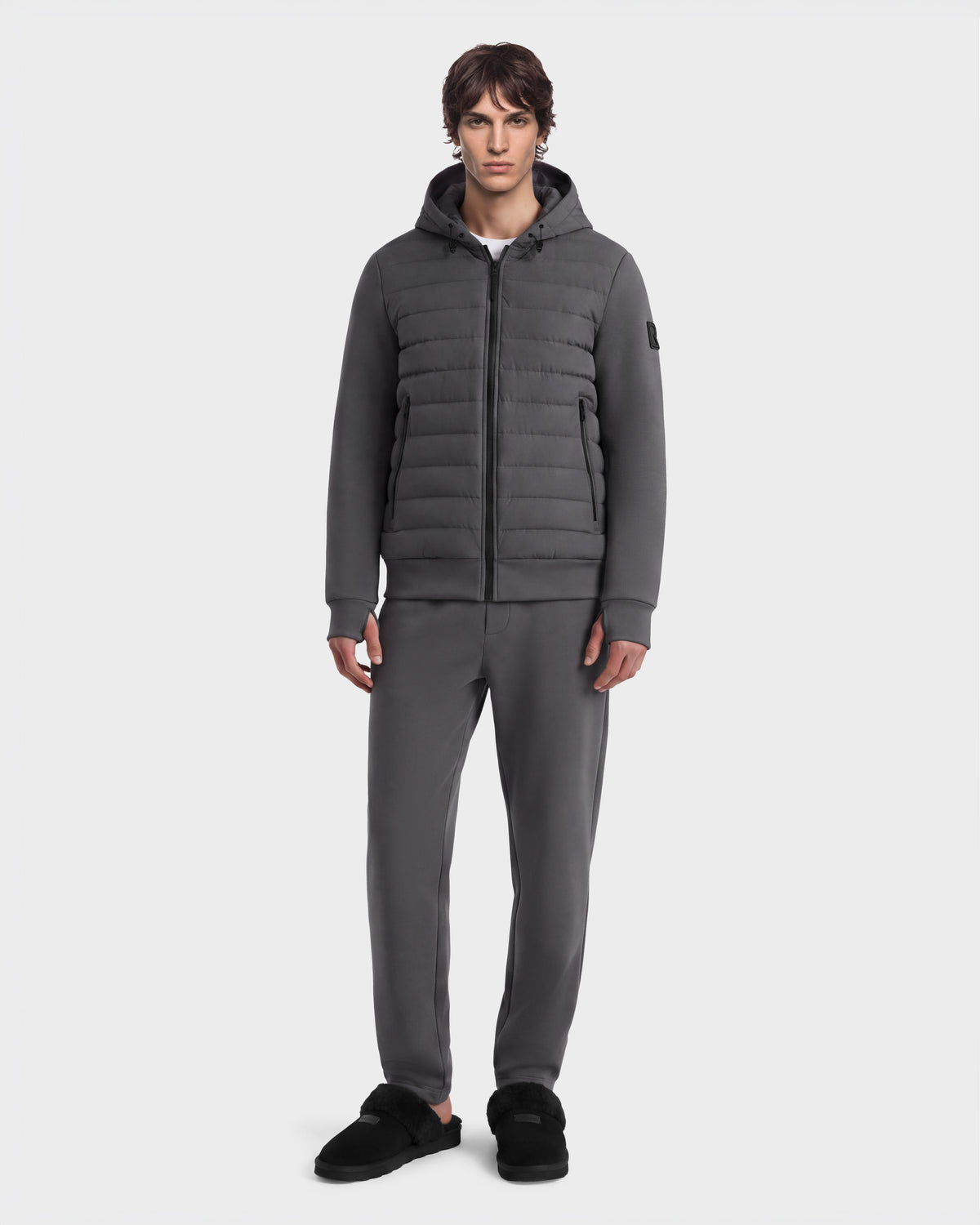 A man wearing the Rudsak DEE MAT - 6124028 Grey urban quilted down jacket with a matching dark grey hooded puffer and sweatpants, paired with black slip-on slippers.