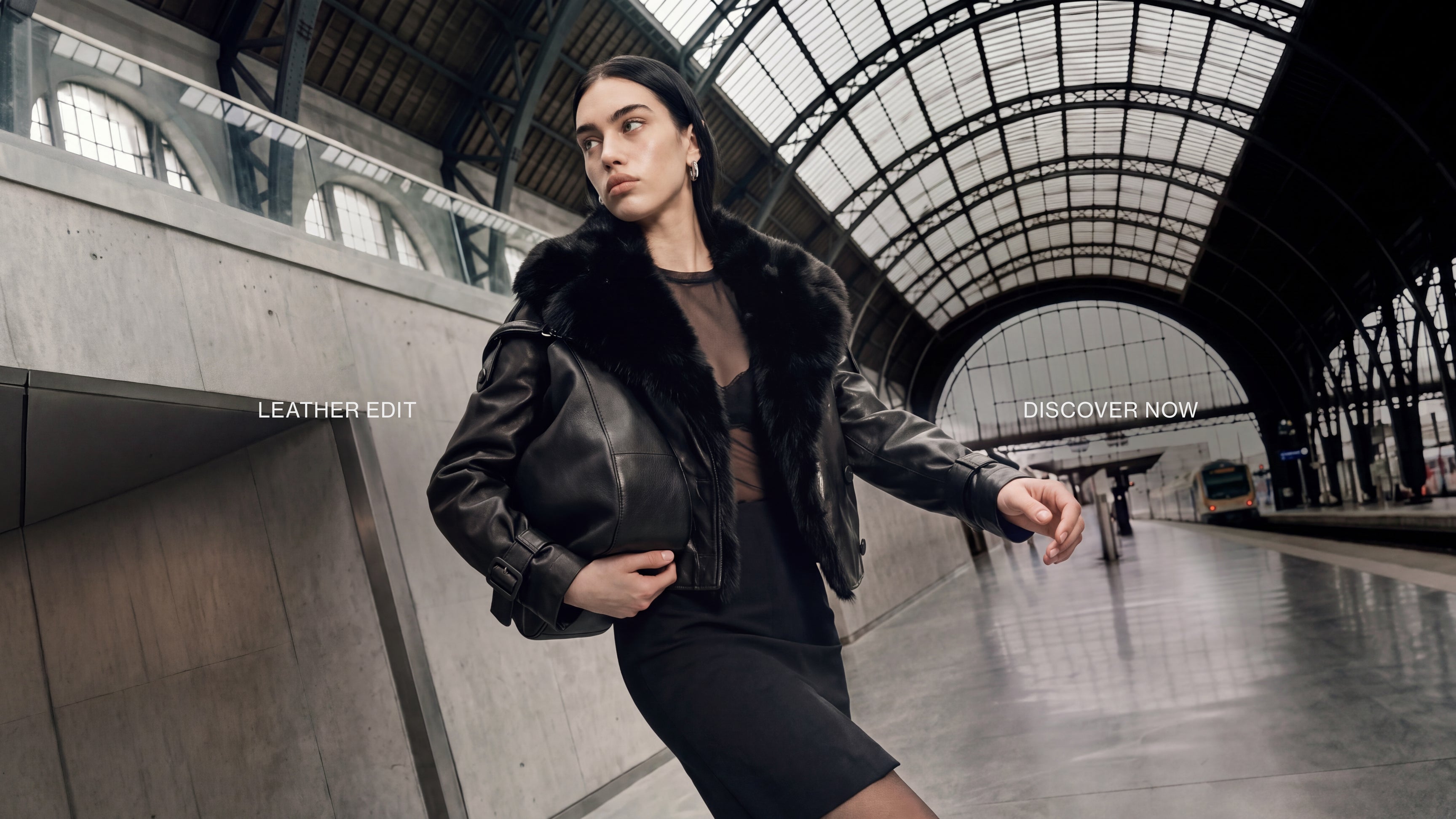 A woman in a black leather jacket with a black fur collar stands in a large, arched train station hall, holding a black leather handbag. French text overlays read 'EDITION OUR' and 'RECHERCHE MAINTENANT'.