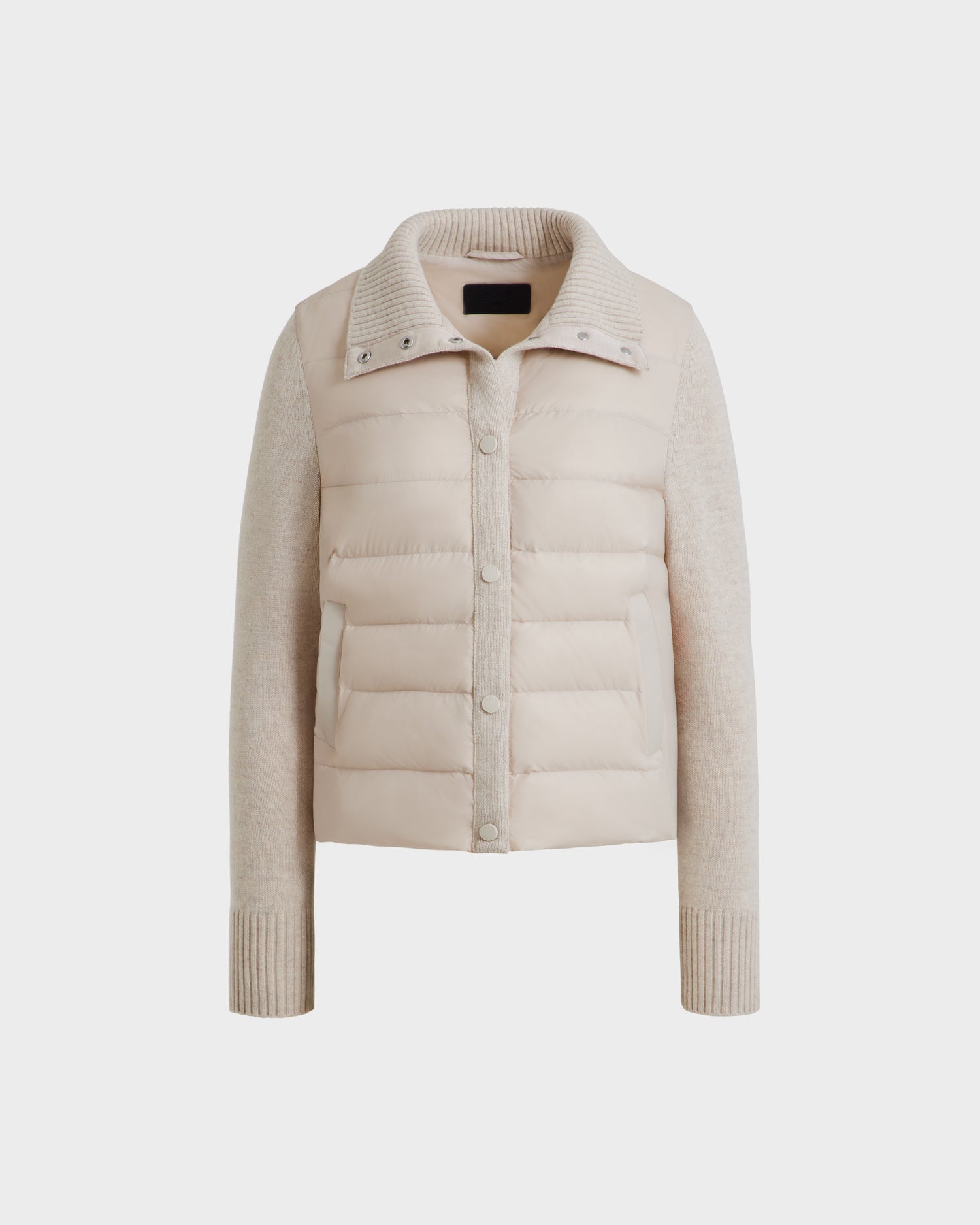 The Rudsak ELLIE - 8125635 Vanilla is a beige women’s long-sleeve quilted down jacket with knit sleeves, ribbed cuffs, and snap-button front—perfect for layering. Shown against a plain white background.