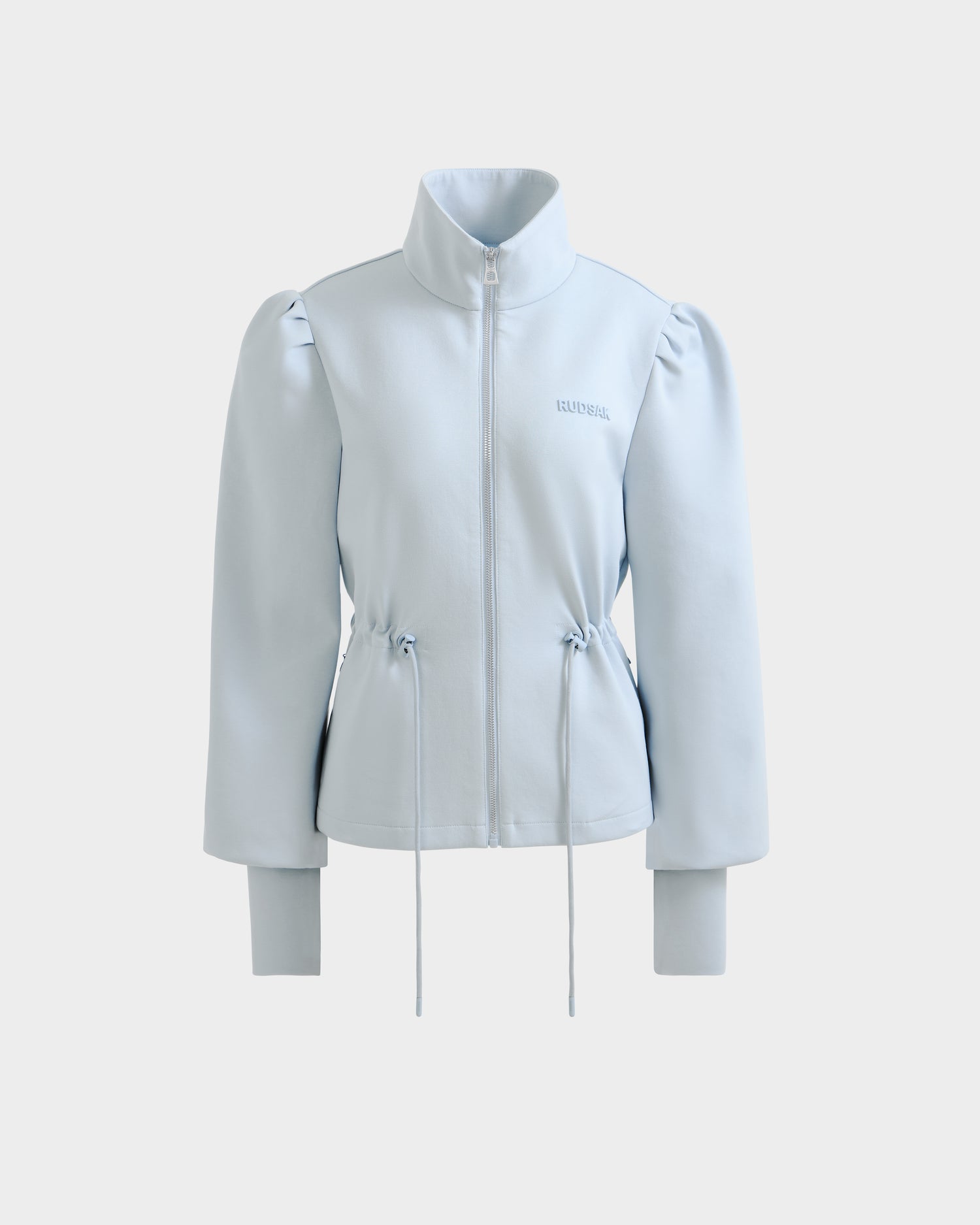 The ELODIE - 8526039 Powder Blue by Rudsak is a light blue zip-up sweater jacket with a high collar, puffed shoulders, long sleeves, and waist drawstrings. Made from a soft stretch cotton blend, it offers a minimal, modern sports-casual style.