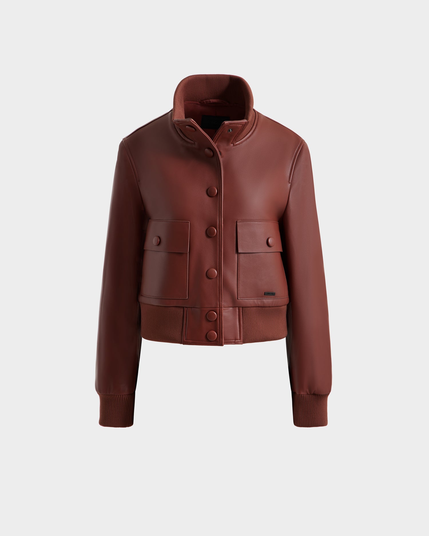 A rust EVERLEIGH - 8125547 women’s leather bomber jacket by Rudsak, featuring a high collar, button front, two chest flap pockets, ribbed cuffs and hem, is displayed on a plain light gray background.