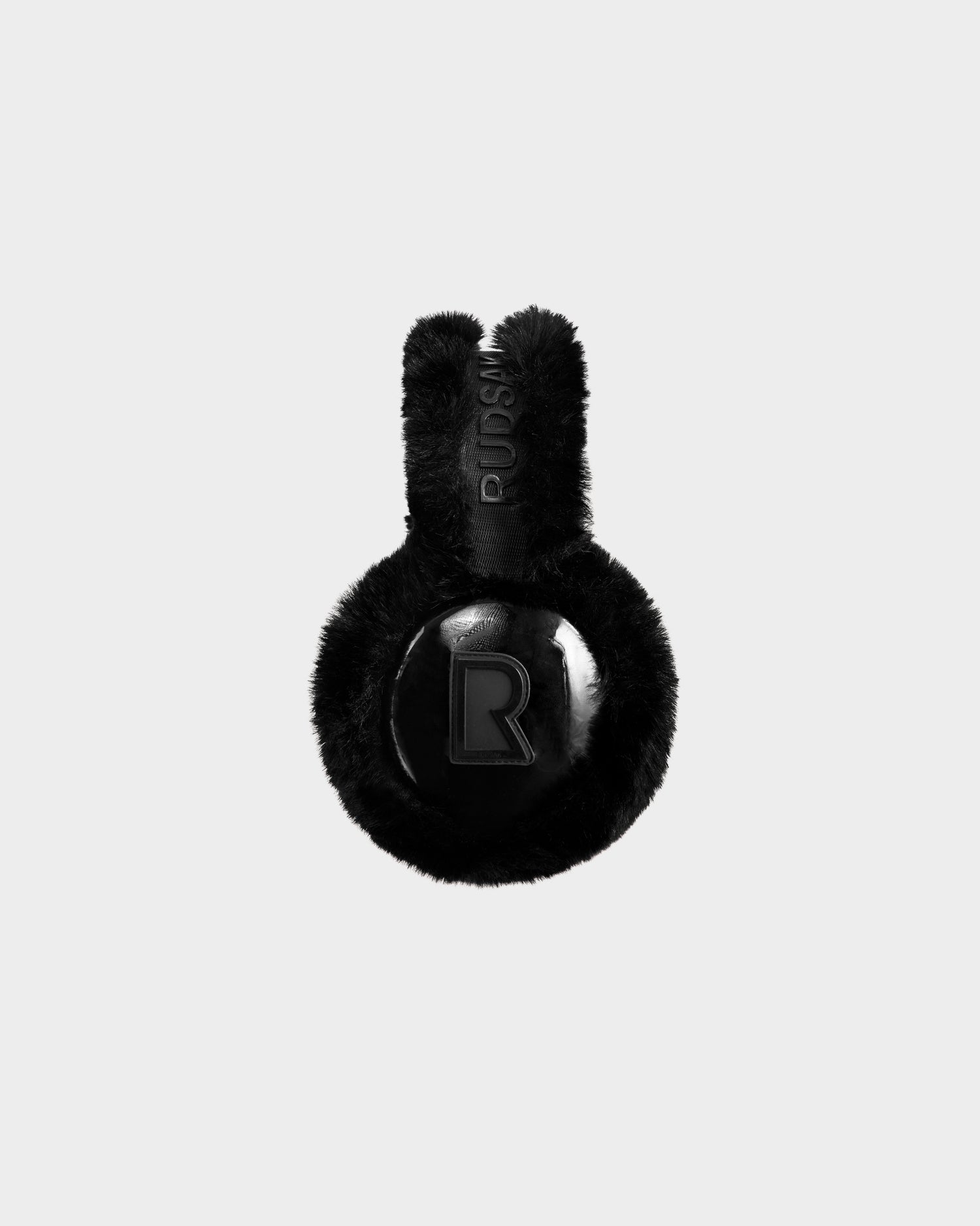 The Rudsak VALENCIA - 8425543 Black earmuffs feature black faux fur, a glossy circular outer panel with a raised R, and "RUSSI" embroidered on the headband—photographed against a plain white background.