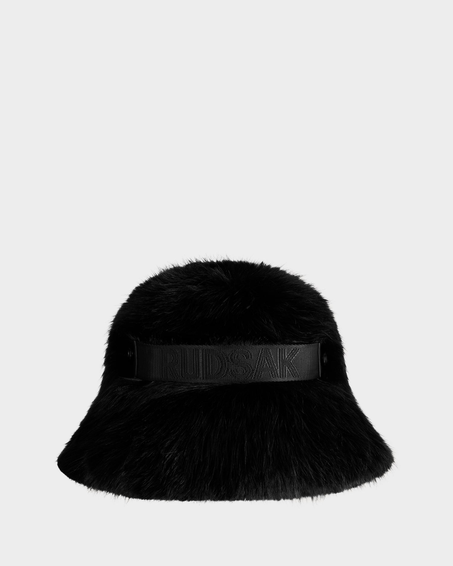 The Rudsak ROMINA - 8425545 Black is a women's black faux fur bucket hat with a wide brim and a leather band embossed with the brand name, shown on a plain light gray background.