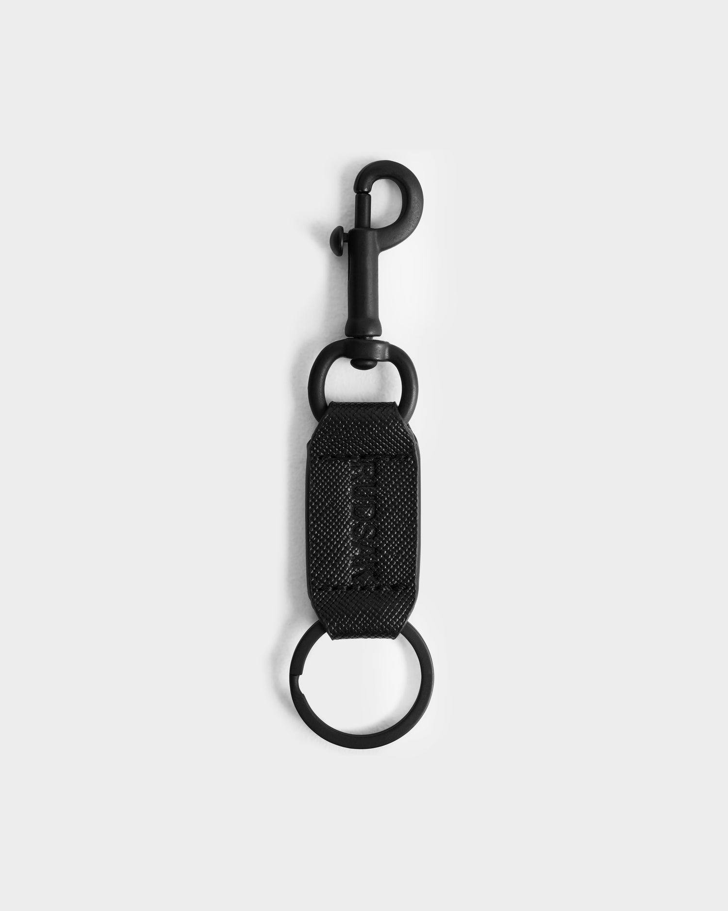 The Rudsak RYLIE - M424500 Black keychain features a snap hook, fabric loop, and round keyring, shown on a light gray background—ideal for pairing with any men’s box set or reversible leather belt.