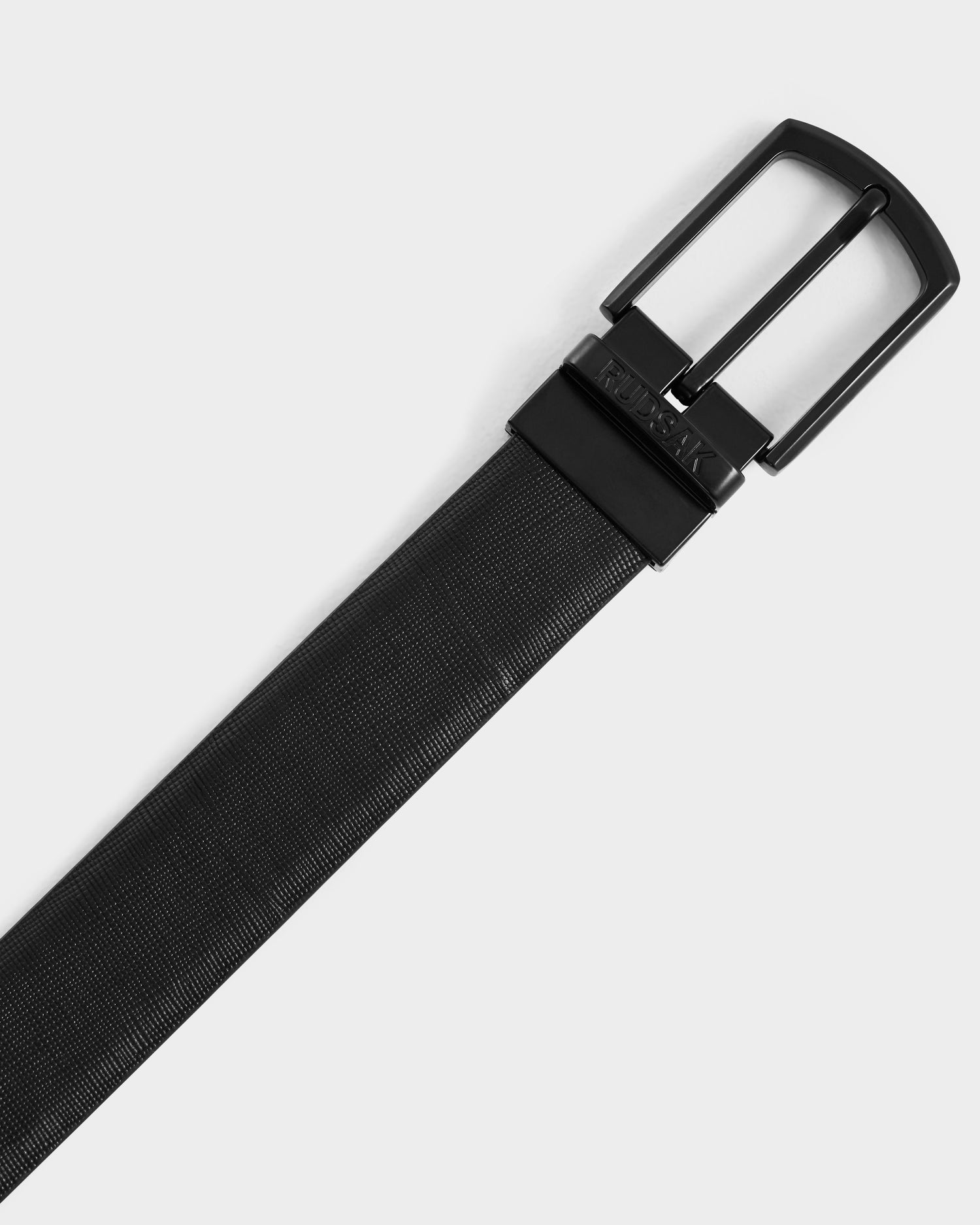 The Rudsak RYLIE - M424500 Black leather belt features a textured pattern and shiny black metal buckle, displayed diagonally on a plain white background—ideal for men’s box sets or gift boxes.
