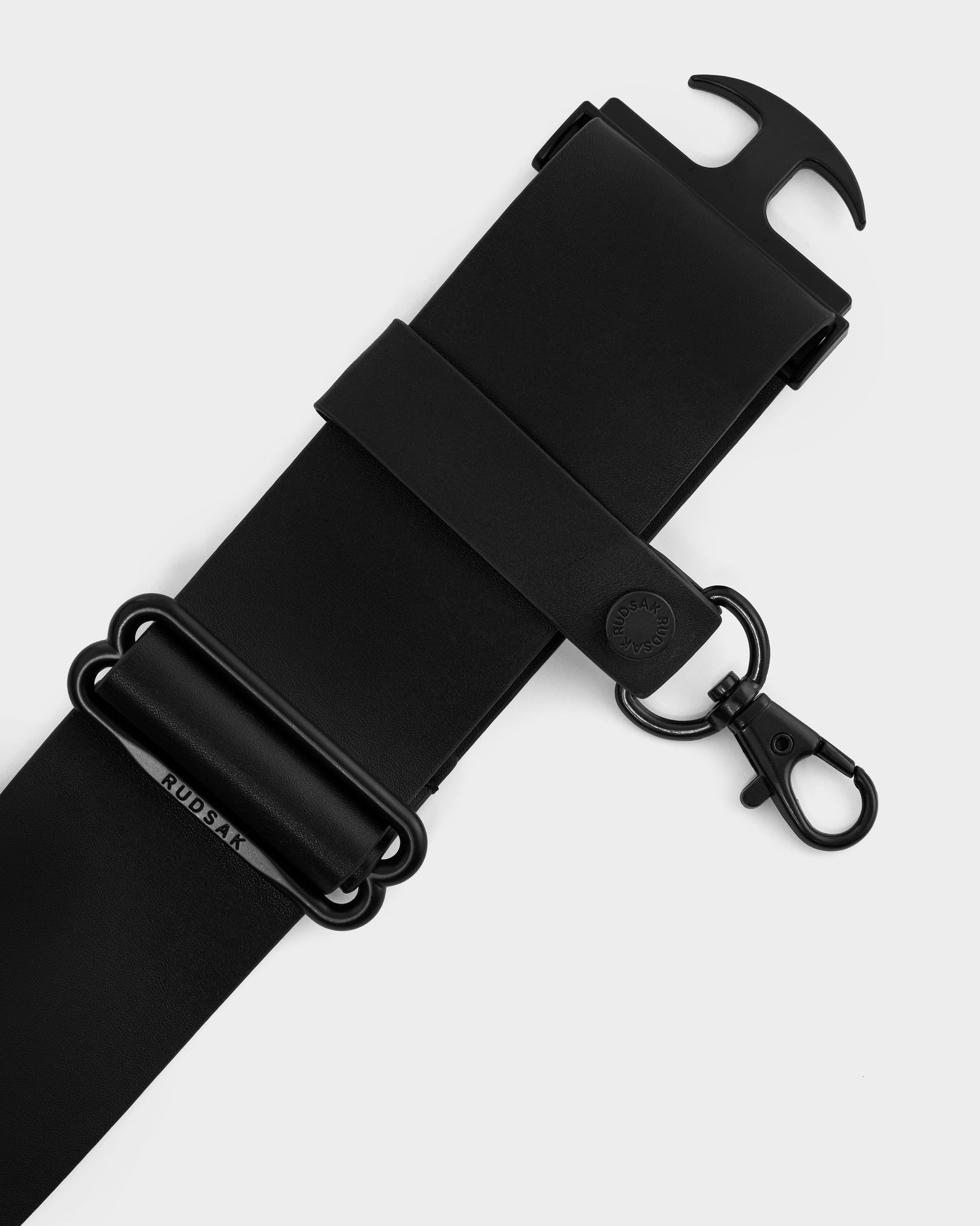 A close-up of the Rudsak LOTUS - 8425002 Black adjustable bag strap with black metal hardware, including a clip and rings. The strap features subtle branding and a button snap detail.