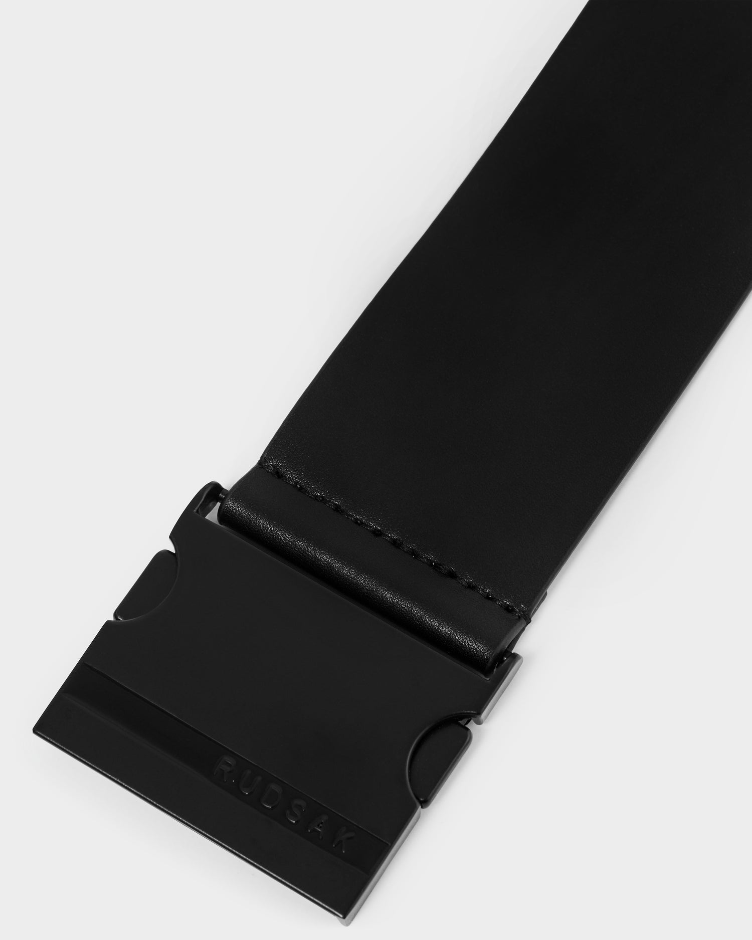 Close-up of the Rudsak LOTUS - 8425002 Black belt in smooth leather with a wide matte black rectangular buckle featuring subtle embossed Rudsak branding.