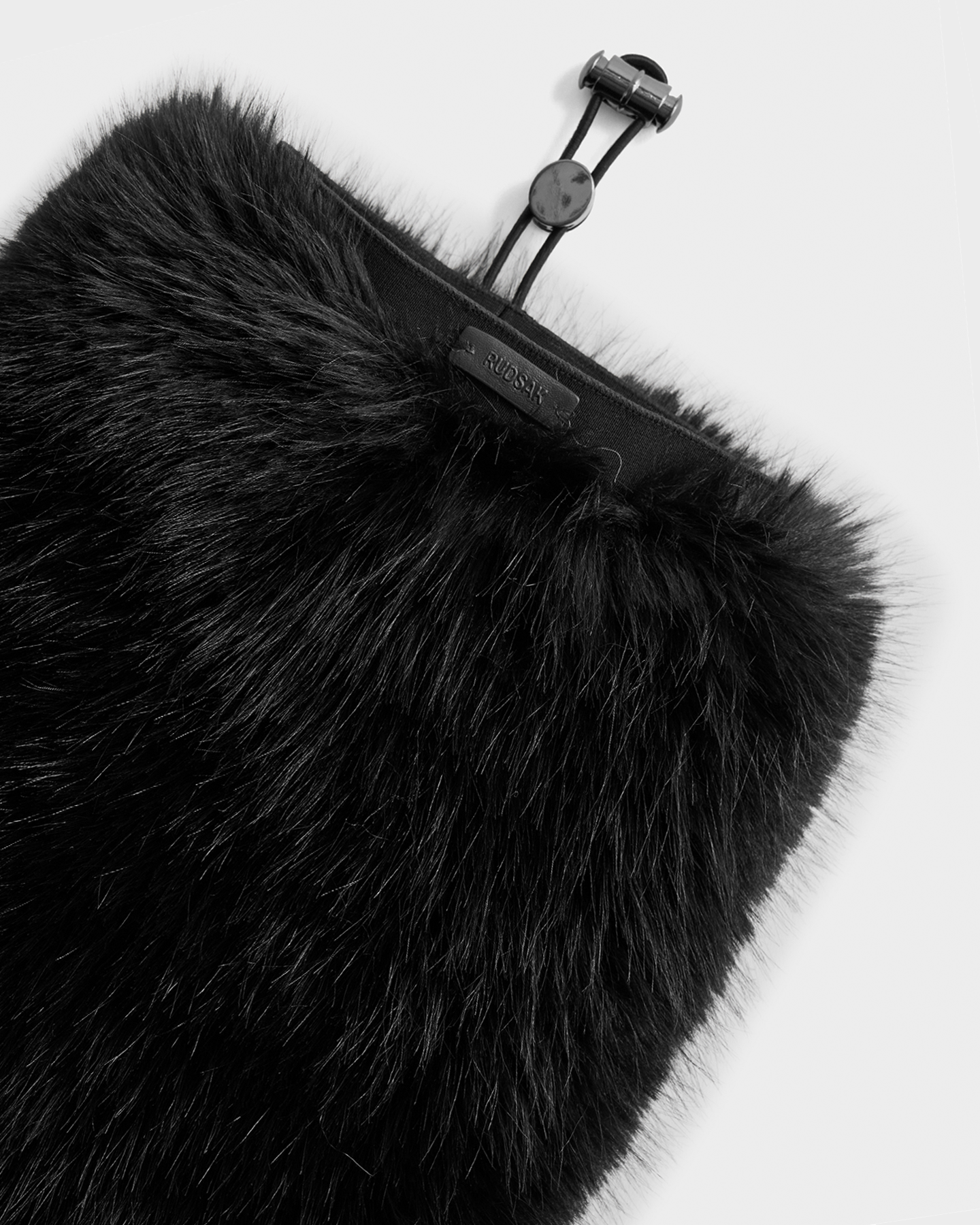 A close-up of the PAIGE - 8425534 Black by Rudsak, a faux fur winter accessory for women featuring a drawstring closure and a leather tag—perfect for après-ski chic style.