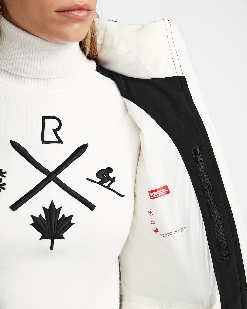 Dressed in the Rudsak ALAIA - 8124816 Iceland ski jacket with RECCO tech, over a white turtleneck sweater with black skiing symbols, only their lower face and torso are visible.