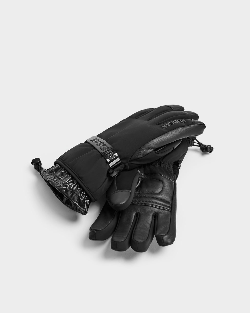 A pair of Rudsak APLEN - 6424505 Black insulated winter gloves with adjustable wrist straps and textured material, shown overlapping on a plain light background.